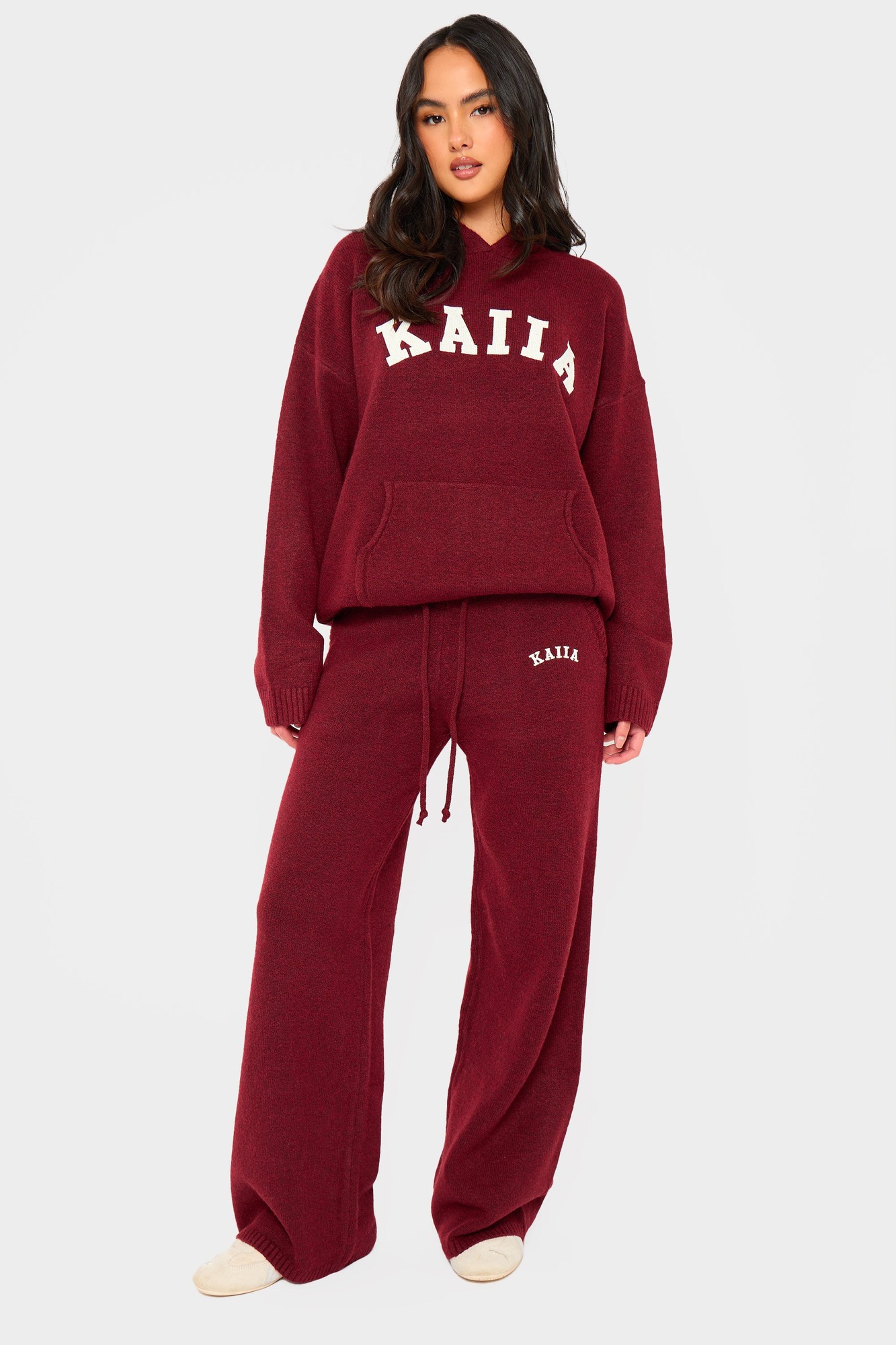 Burgundy wide-leg trousers made from soft knit fabric, featuring an elastic waistband with drawstring and subtle logo detailing on the side.