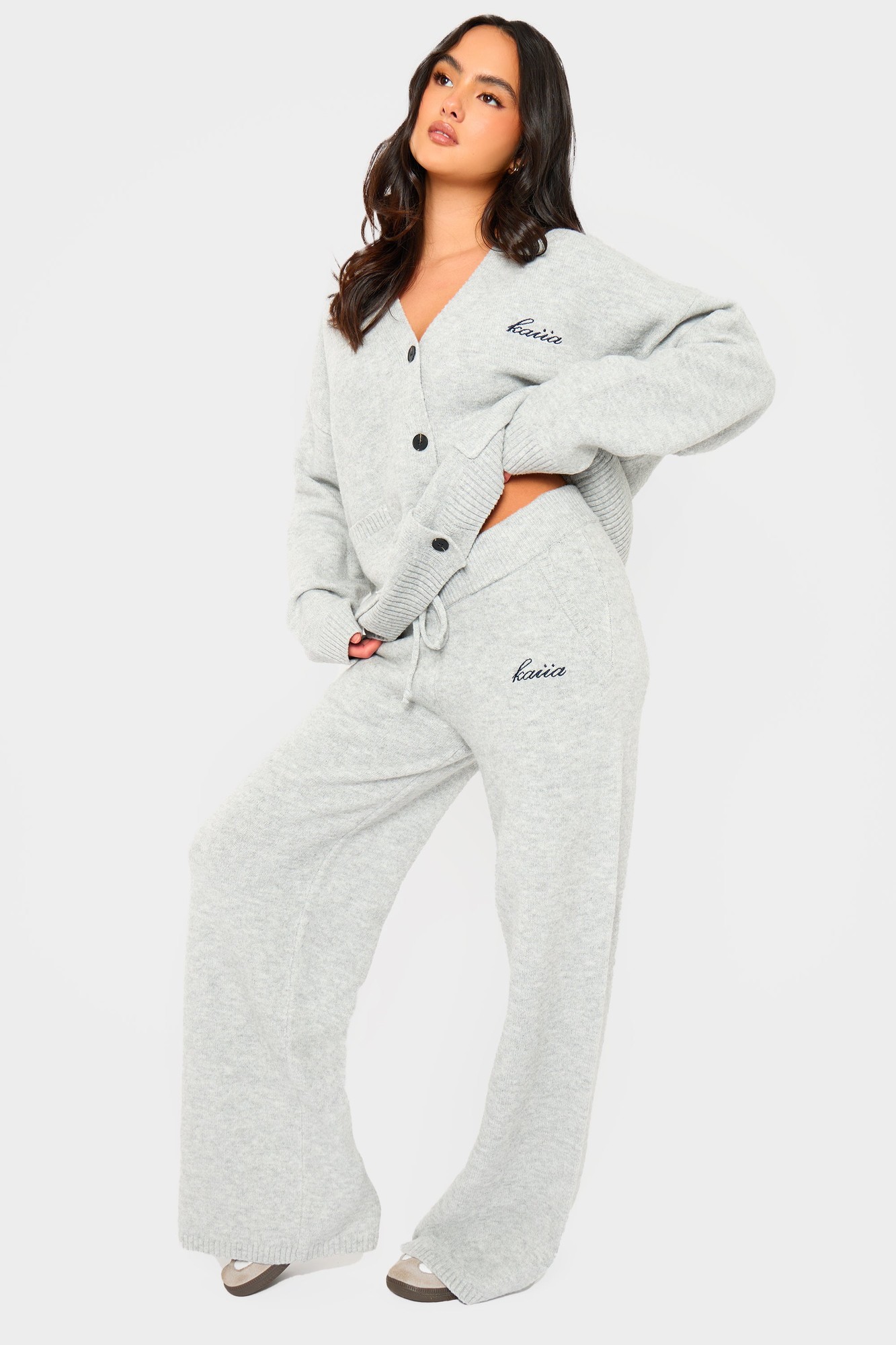 Grey marl wide leg trousers made from soft knit material, featuring a drawstring waist and embroidered branding on the side, styled with a matching cardigan.
