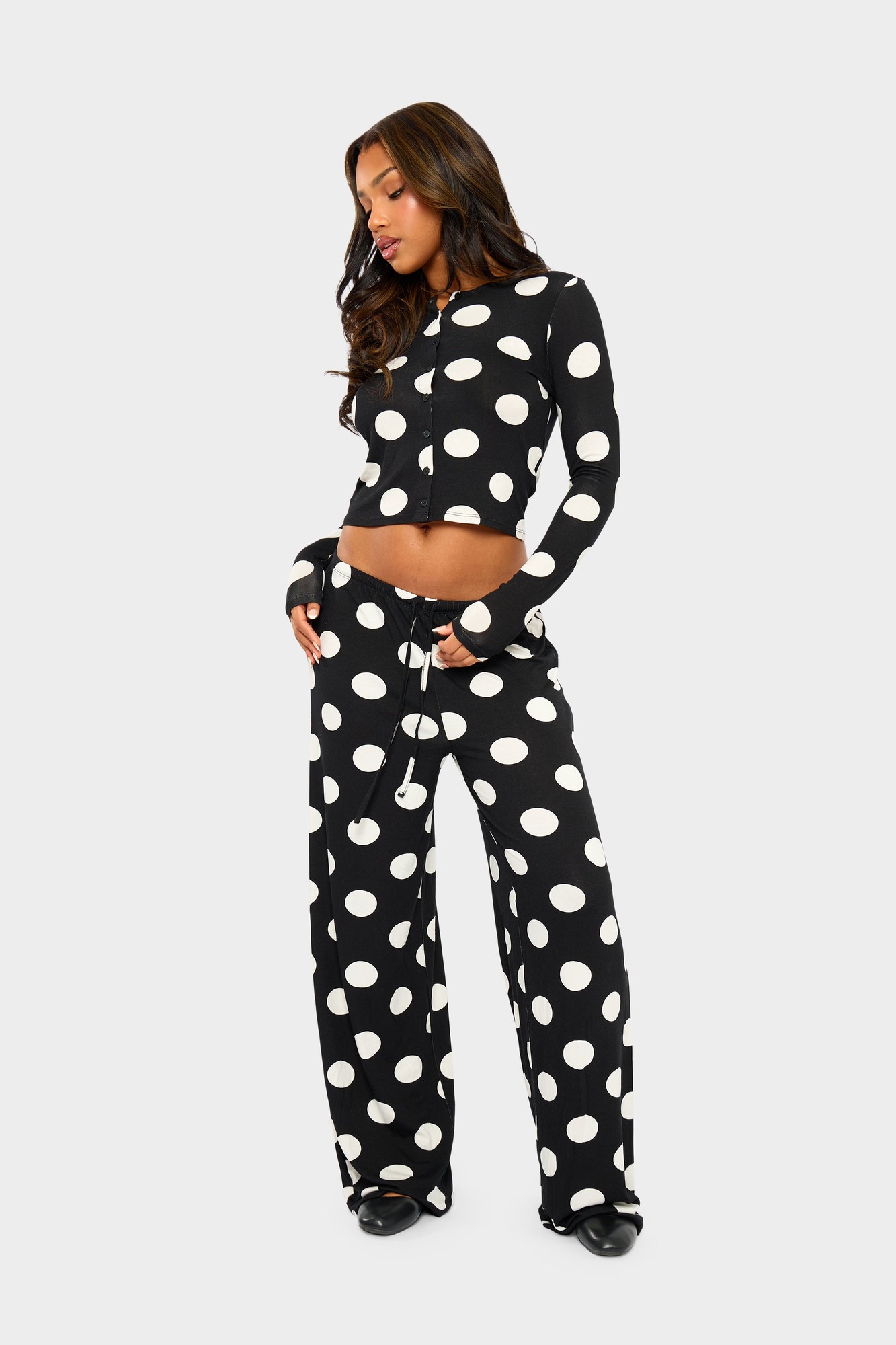 Black wide-leg trousers featuring large cream polka dots, made from soft material, styled with an elastic waistband and drawstring for a comfortable fit.