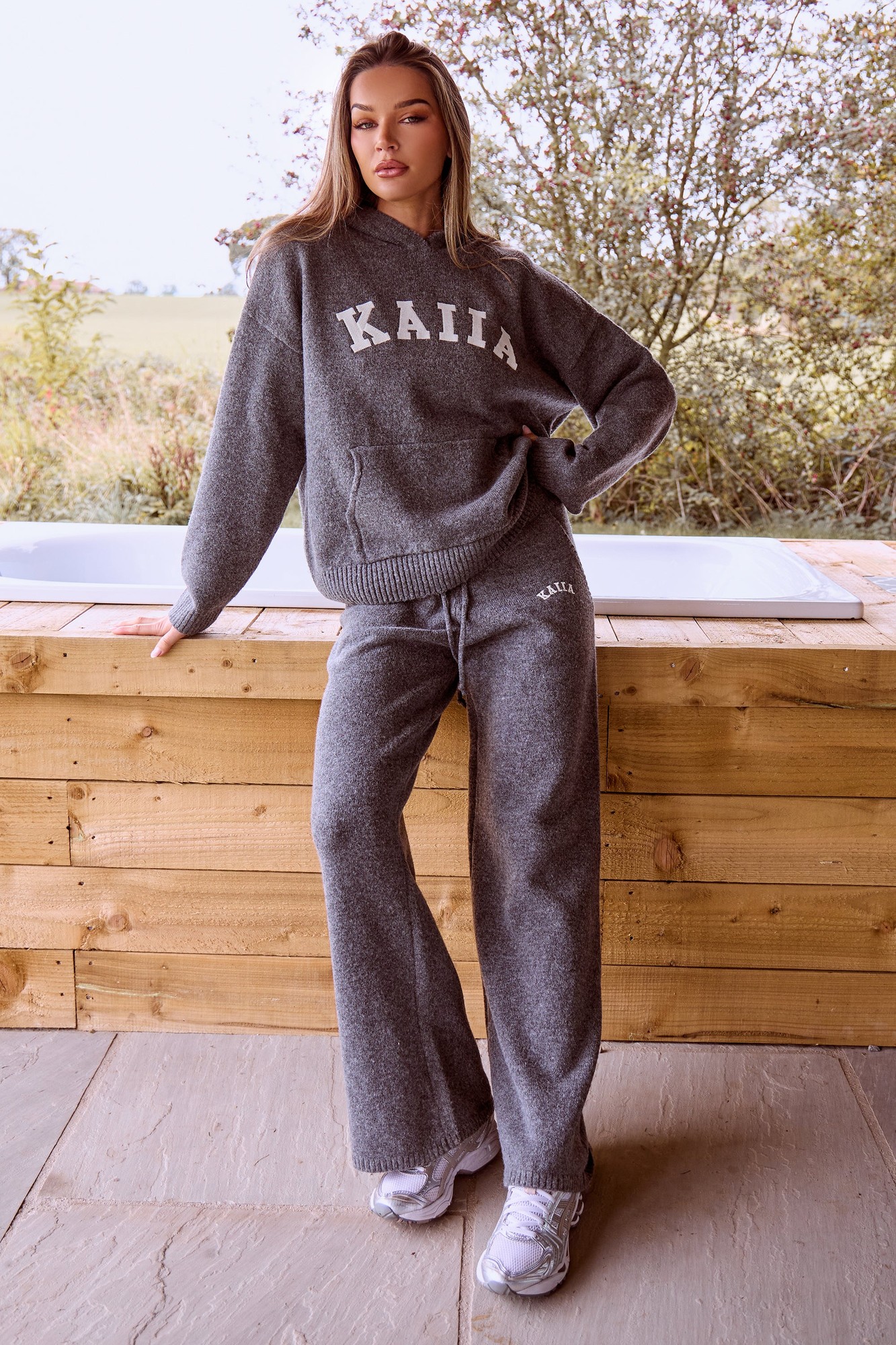 Charcoal wide-leg trousers made of soft knit material, featuring the "Kaiia" logo in white, paired with a matching sweatshirt, set against a natural outdoor backdrop.