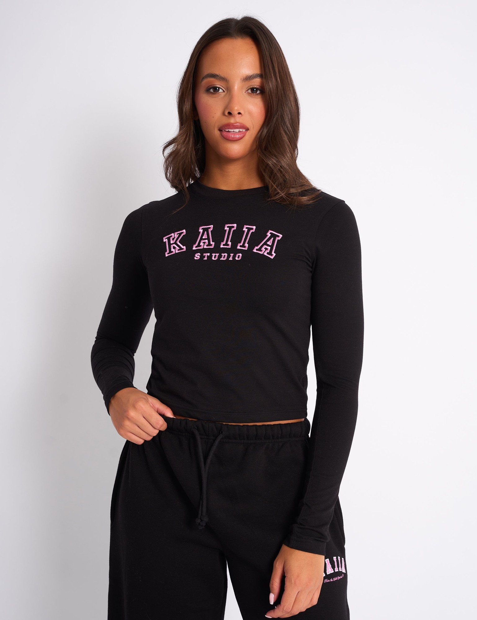 Black long sleeve baby tee featuring the "KAIIA" logo in pink across the chest, made from a soft, stretchy material, styled with a fitted silhouette.