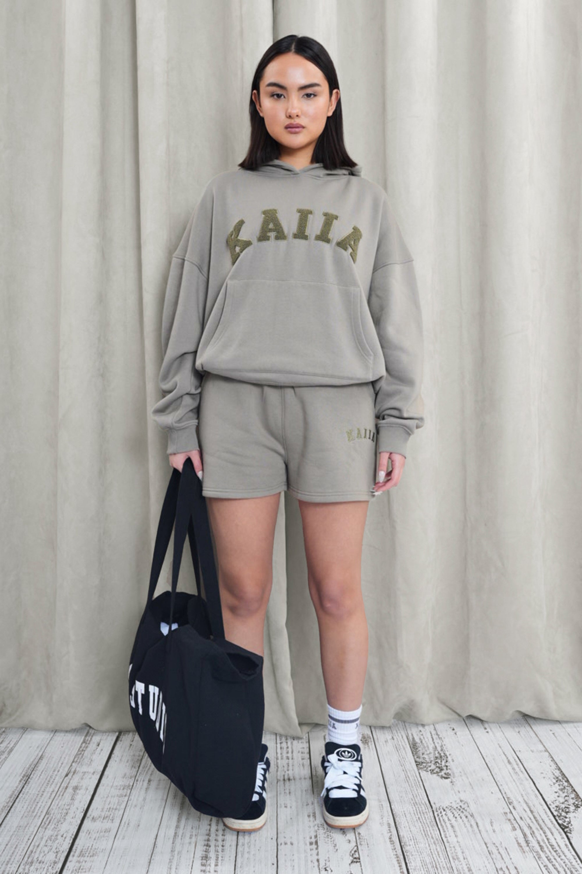 Khaki sweat shorts by Kaiia, featuring a comfortable fit, soft material, and the brand logo embroidered on the front, styled with a matching oversized sweatshirt and black tote bag.