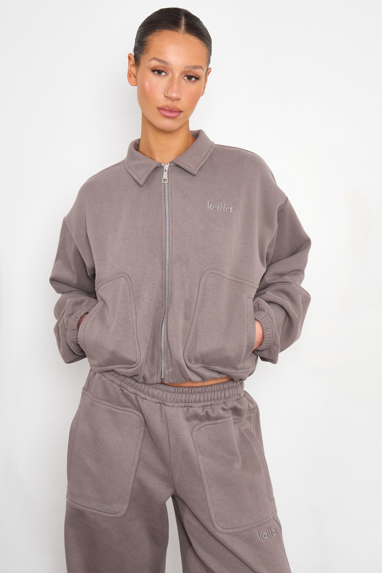 Silver grey zip-through sweatshirt with a collared neckline, featuring large front pockets and the brand name "Kaiia" embroidered on the chest.