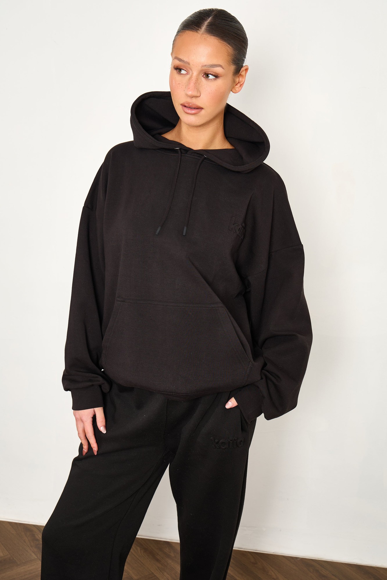 Black oversized hoodie made from premium scuba material, featuring a drawstring hood, front pocket, and relaxed fit, styled with matching black pants.