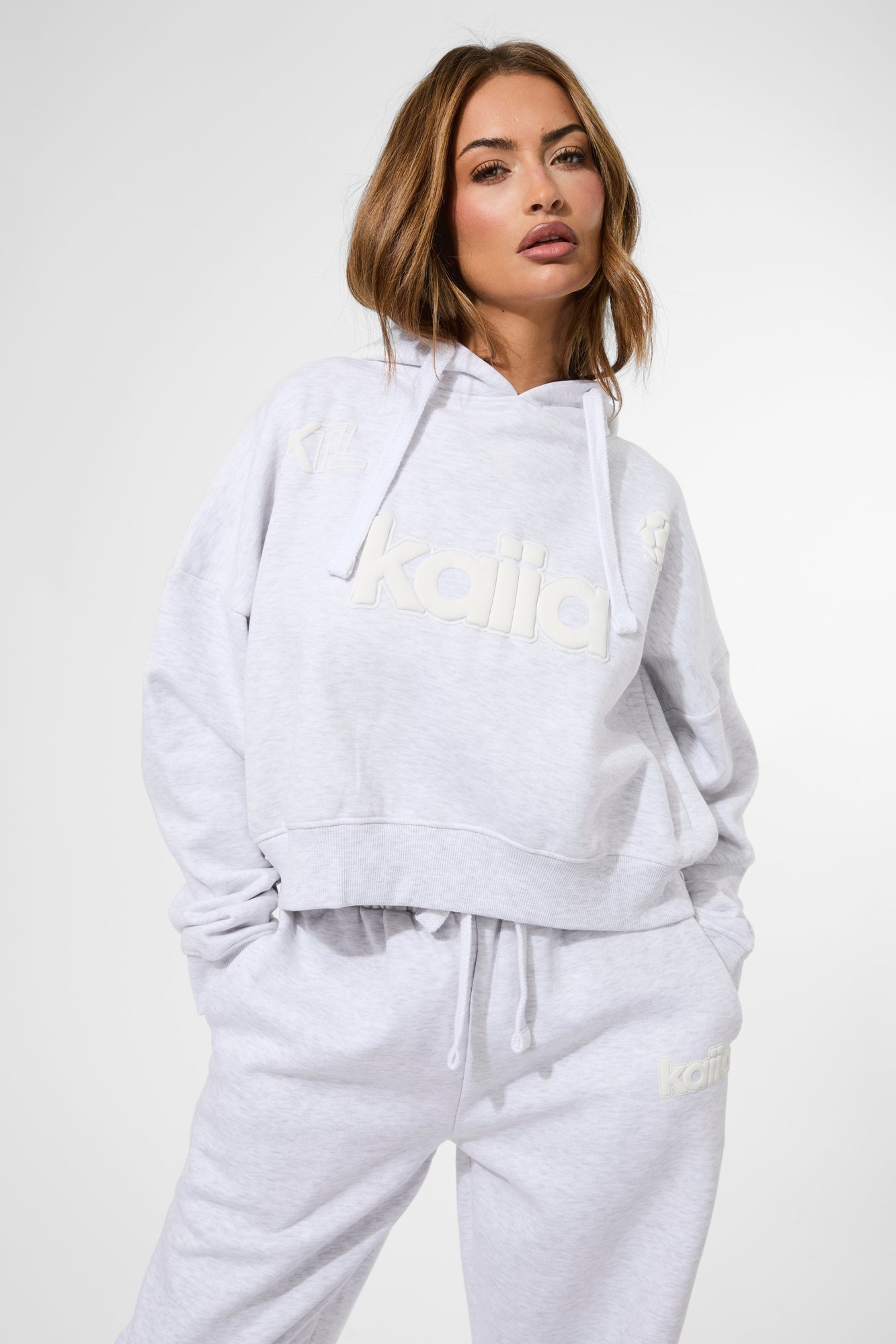 Cropped oversized hoodie in ash grey marl featuring a puff print logo, drawstring hood, and relaxed fit, styled with matching sweatpants.