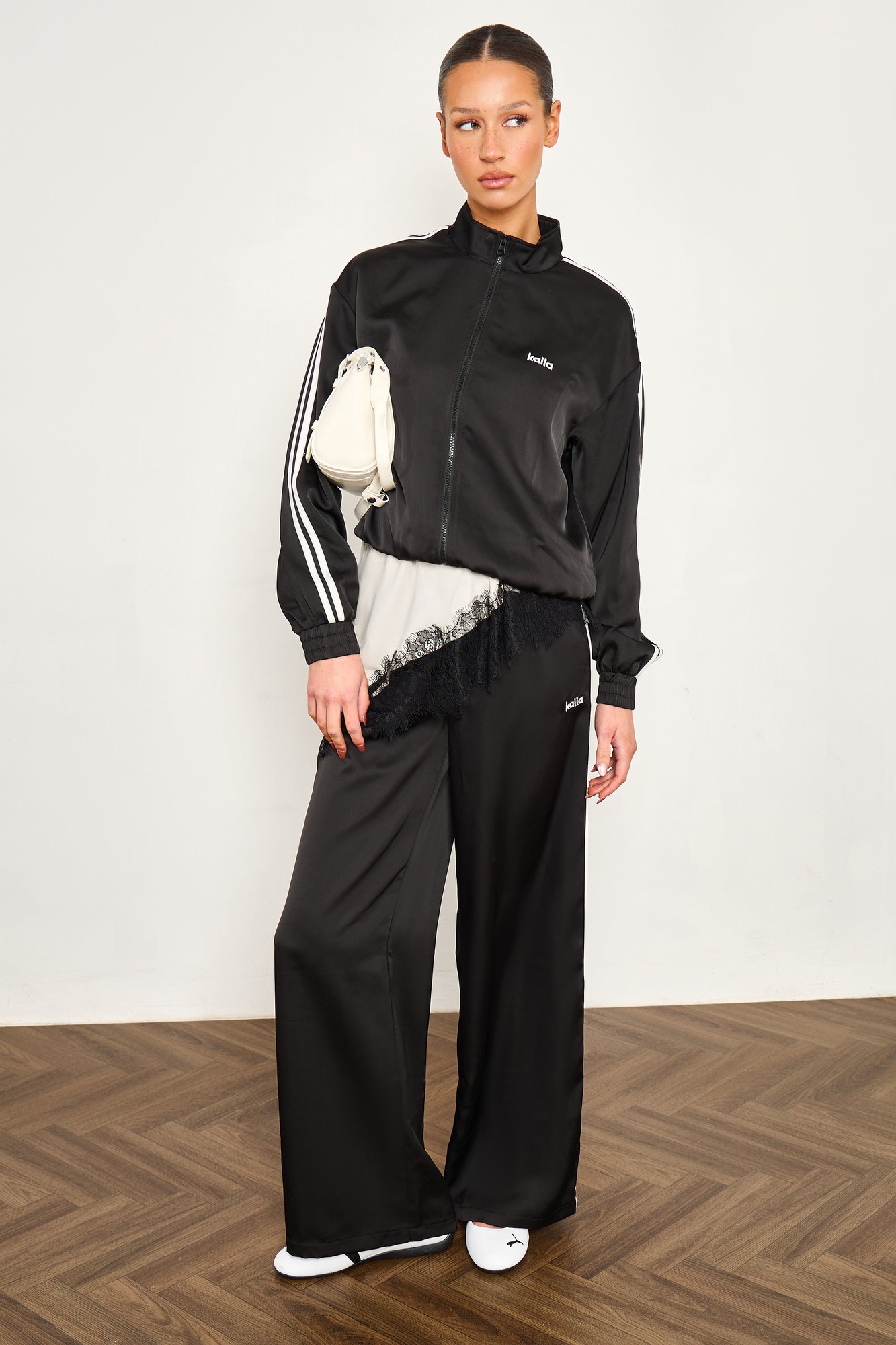 Black satin wide leg trousers with white side stripes, featuring a smooth finish and a relaxed fit, styled with a matching black jacket and white accessories.