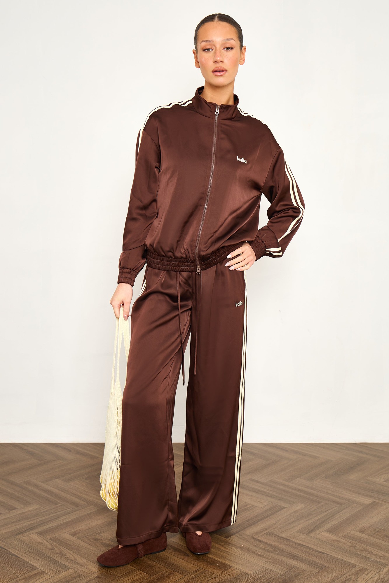 Cocoa brown satin wide leg trousers with lemon side stripes, featuring an elastic waistband and a relaxed fit, styled with a matching zip-up jacket.