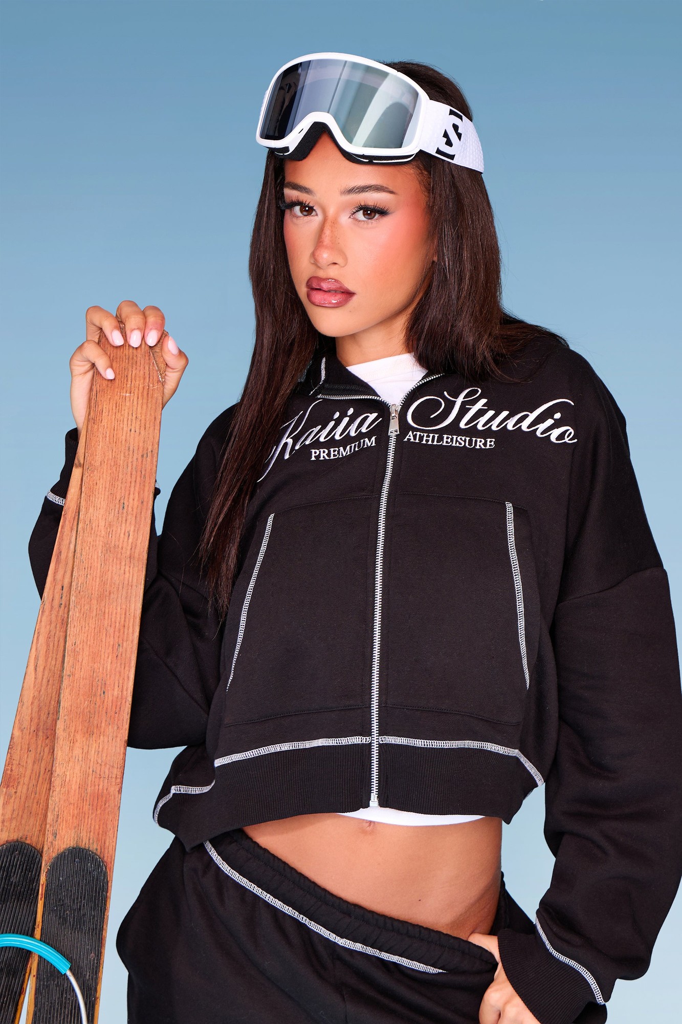 Black and white oversized zip-through hoodie featuring contrast stitching, with "Kaiia Studio" branding, paired with sporty accessories and a ski board.