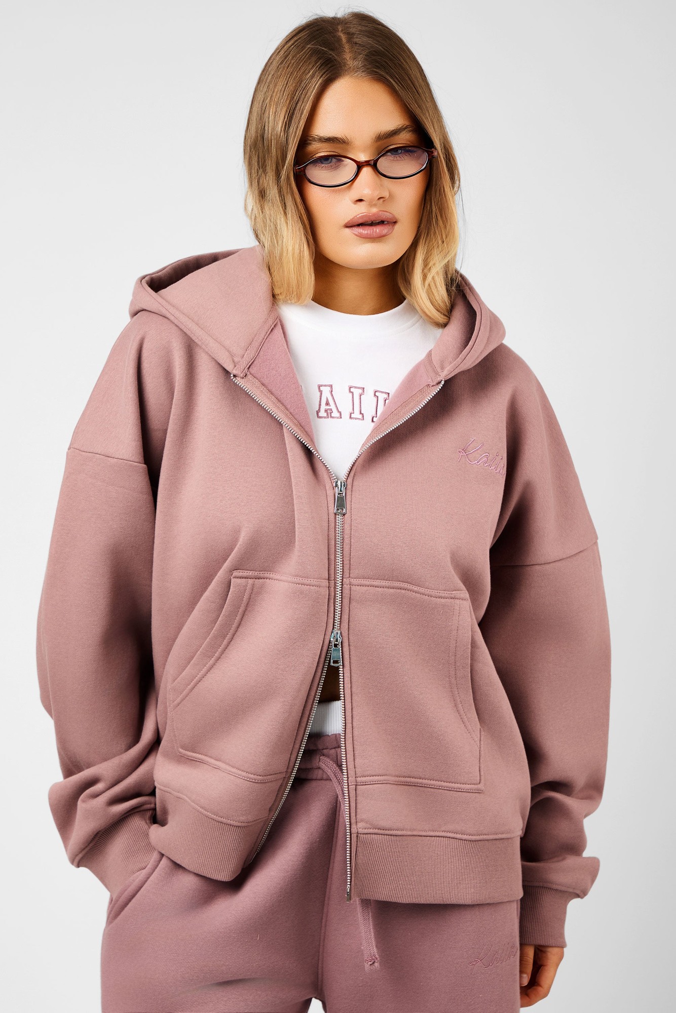 Oversized rosewood hoodie featuring a double-ended zip, front pockets, and embroidered "Kaiia" logo, styled with a white tee and matching sweatpants.