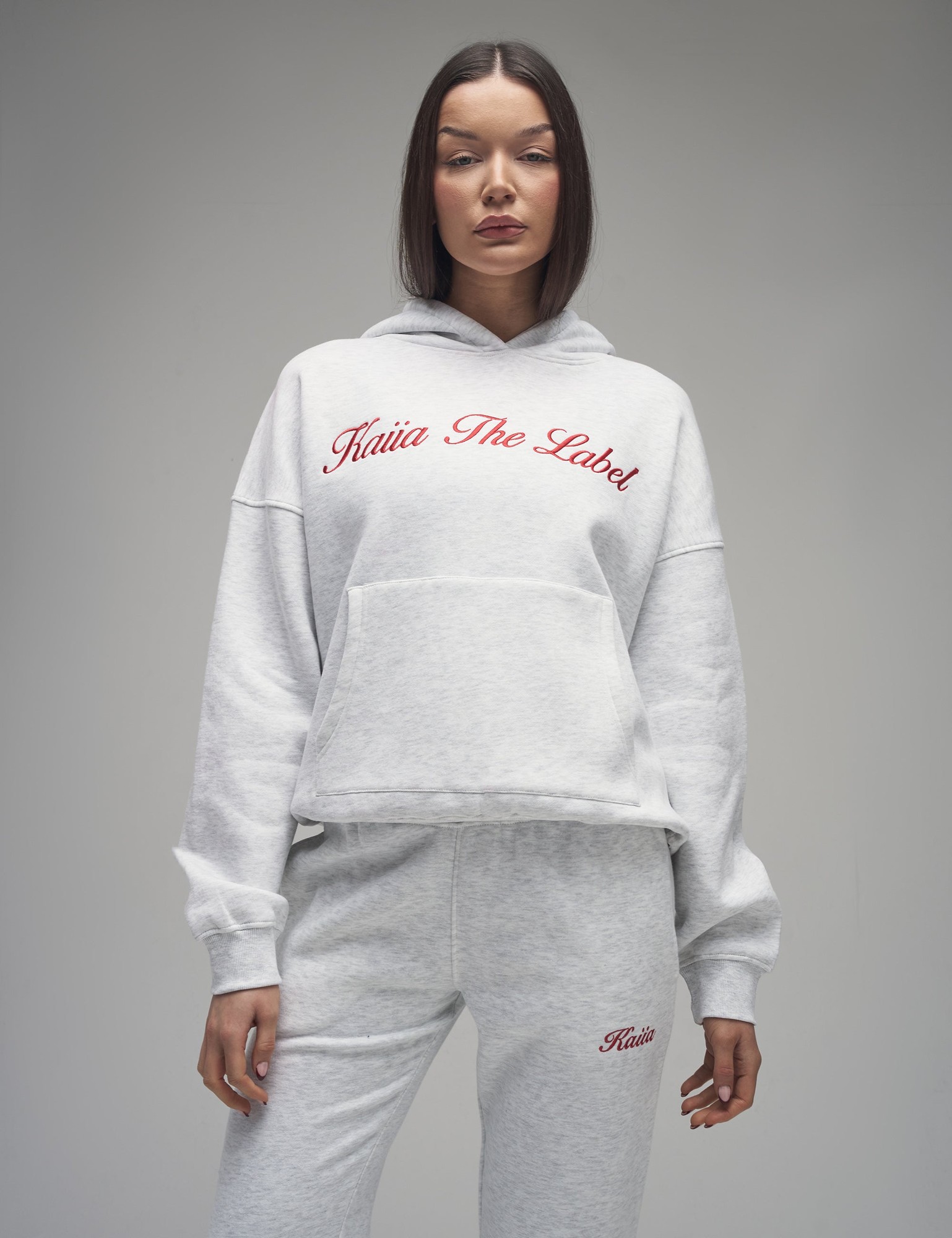 Oversized light grey marl hoodie featuring a red embroidered "Kaiia The Label" logo and a front pocket, styled with matching grey sweatpants.