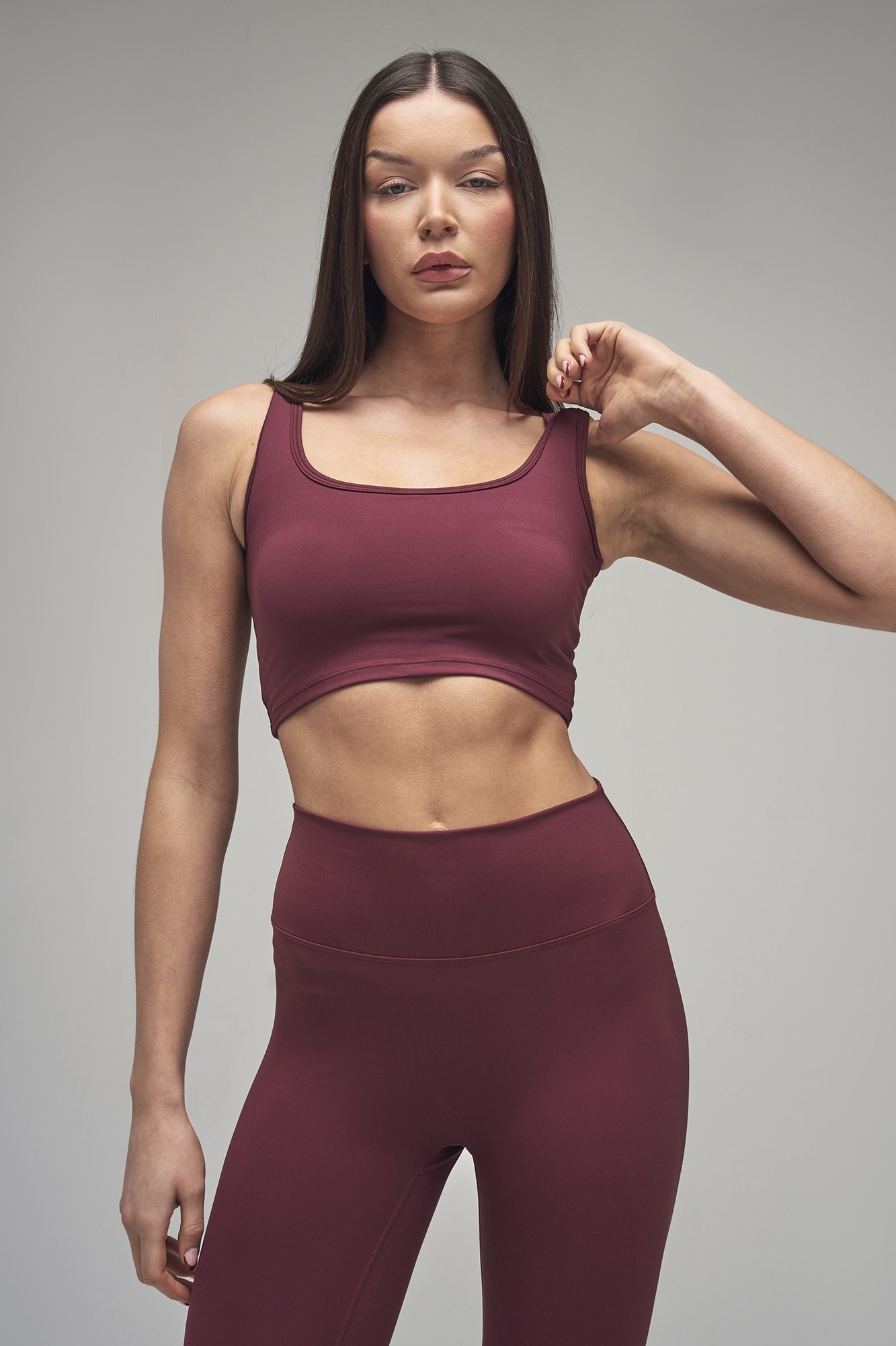 Dark cherry square neck crop top with a fitted design, made from a stretchy material, paired with high-waisted leggings, showcasing a sleek and modern silhouette.