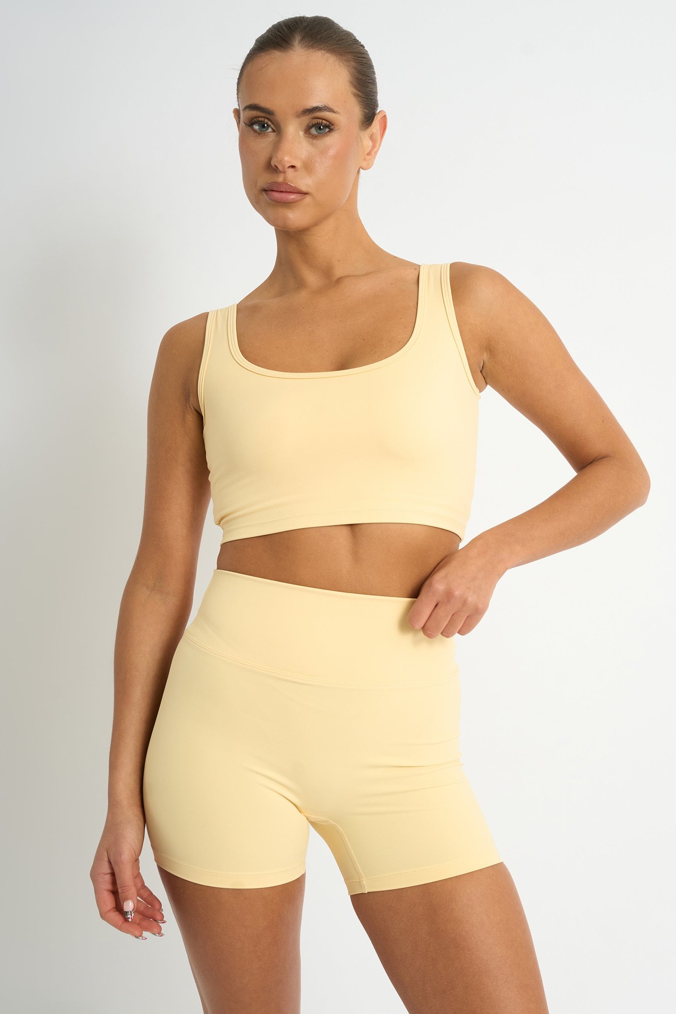 Yellow square neck crop top with a fitted design, featuring wide straps and a smooth, stretchy material, paired with matching high-waisted shorts.