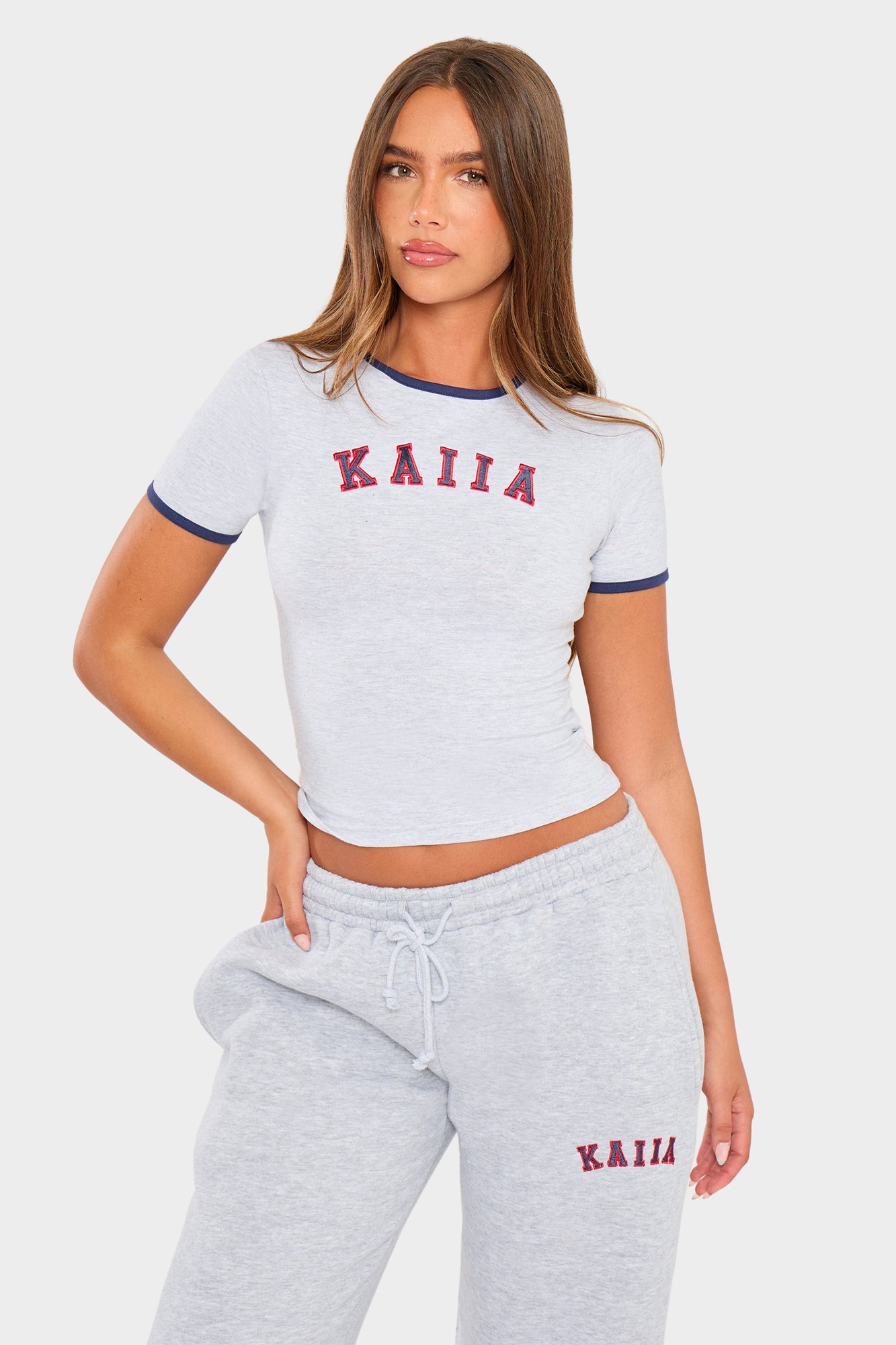 Light grey marl baby tee with red "KAIIA" slogan, featuring a fitted design and contrasting navy blue trim around the neckline and sleeves, styled with matching grey sweatpants.