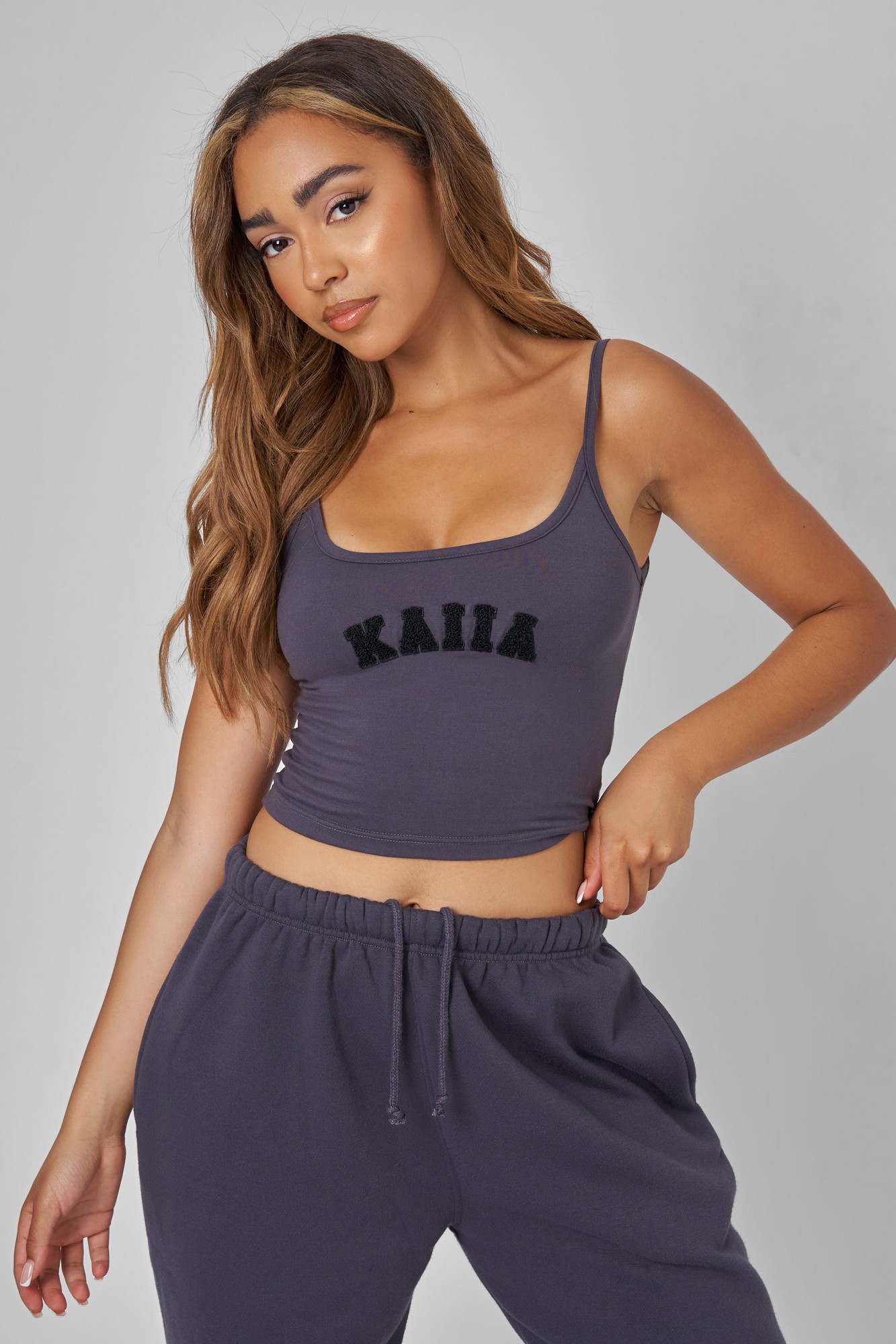 Dark grey slogan vest top featuring the word "KAIIA" in textured black lettering, with thin straps and a fitted design, paired with matching joggers.