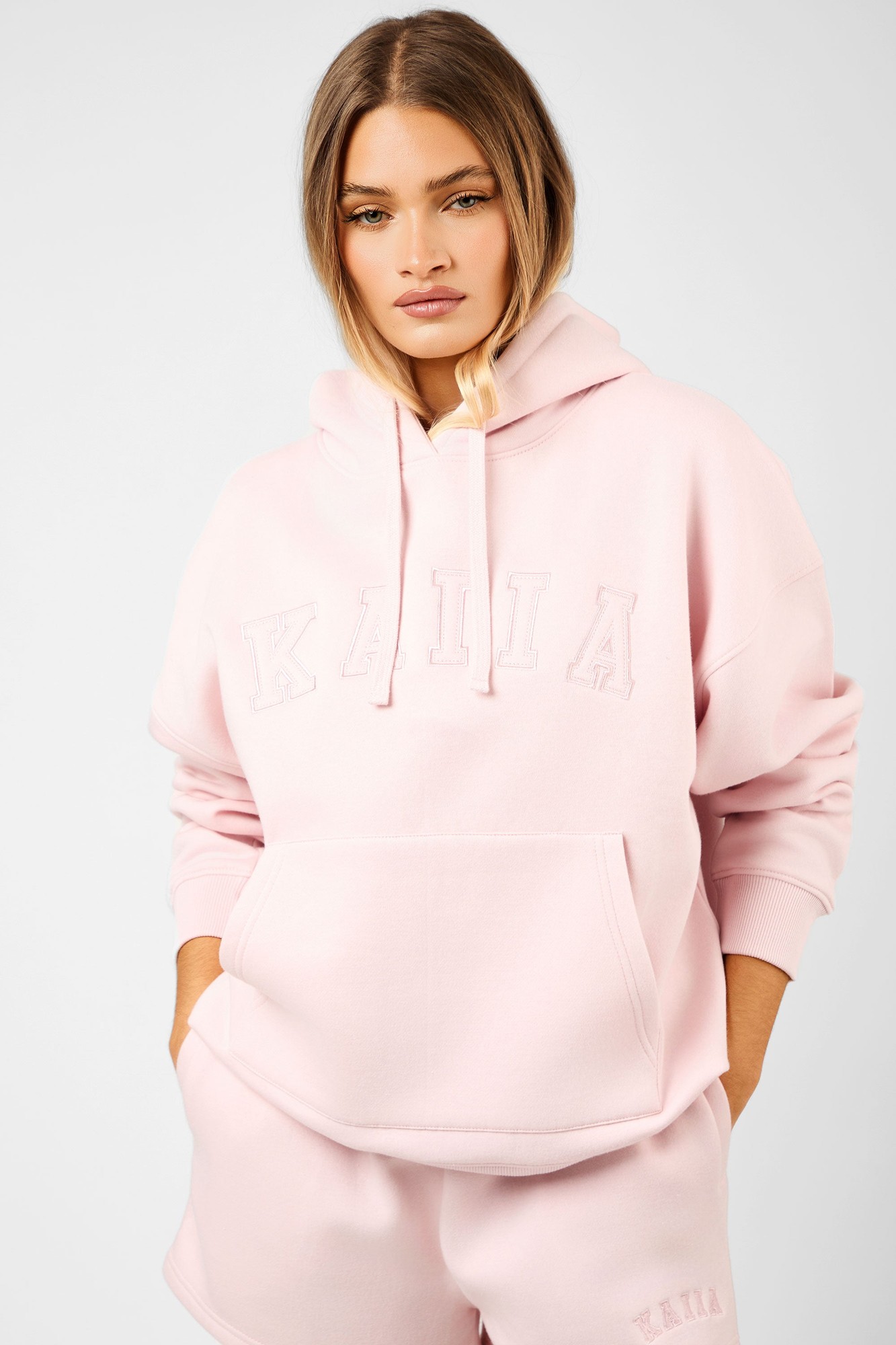 Oversized dusty pink hoodie featuring a drawstring hood, front pocket, and embossed "KAIIA" slogan on the chest, made from soft, comfortable material.