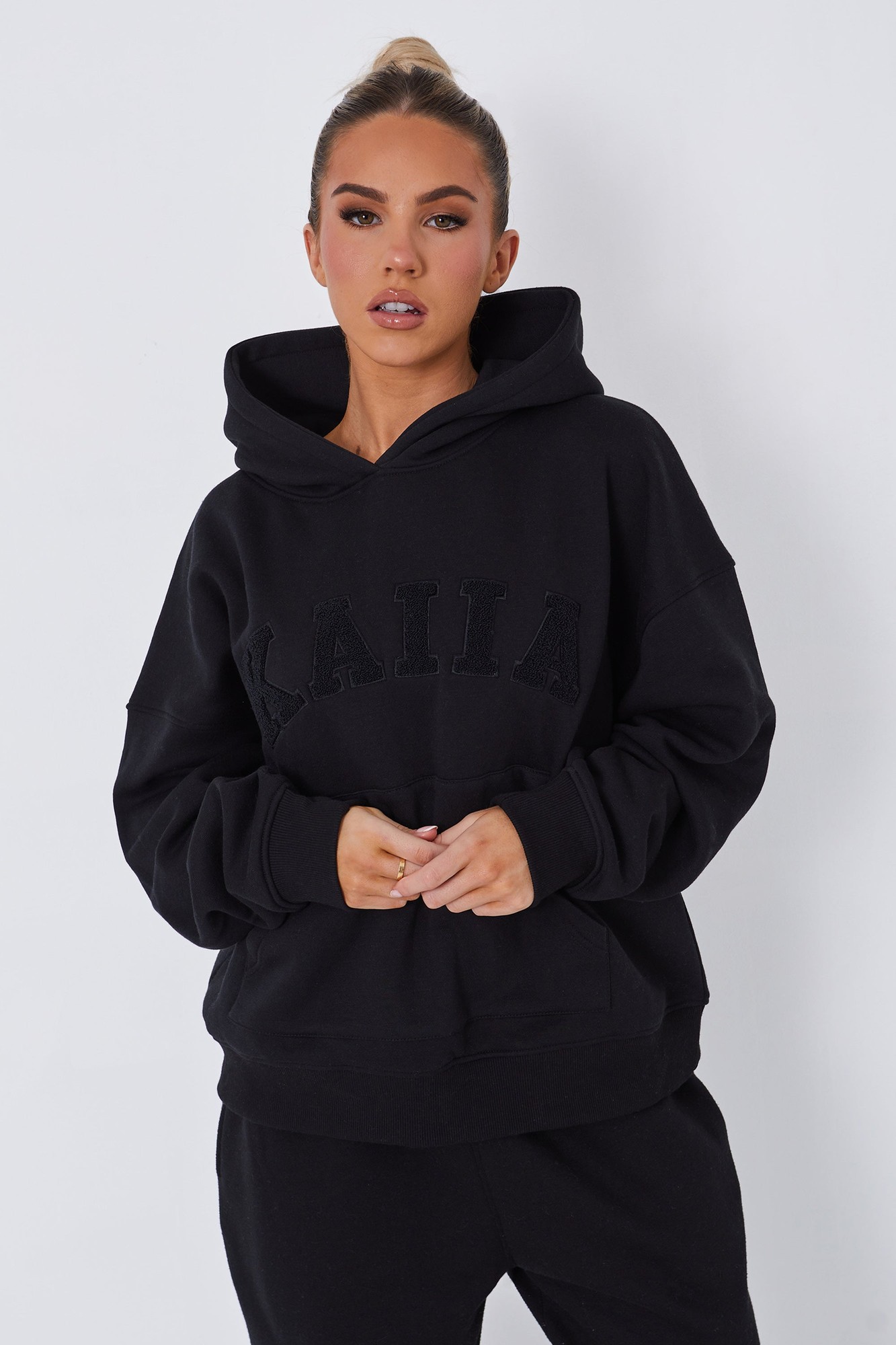 Oversized black hoodie featuring a textured black "KAIIA" slogan across the chest, with a spacious hood and front pocket, made from soft, comfortable fabric.