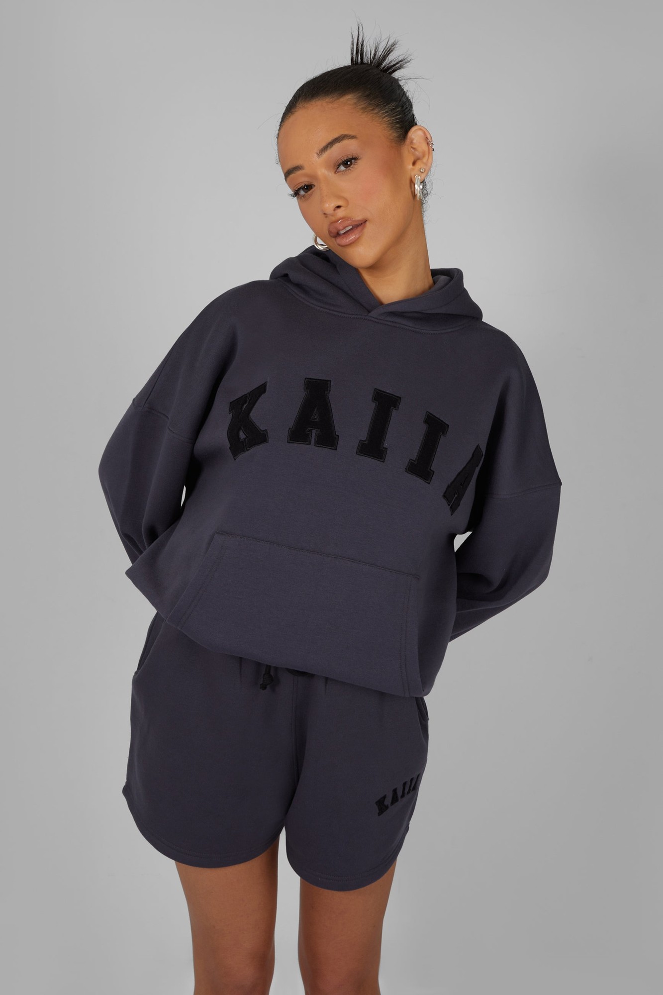 Oversized dark grey hoodie featuring a black "KAIIA" slogan across the front, made of soft material, styled with a relaxed fit and a drawstring hood.