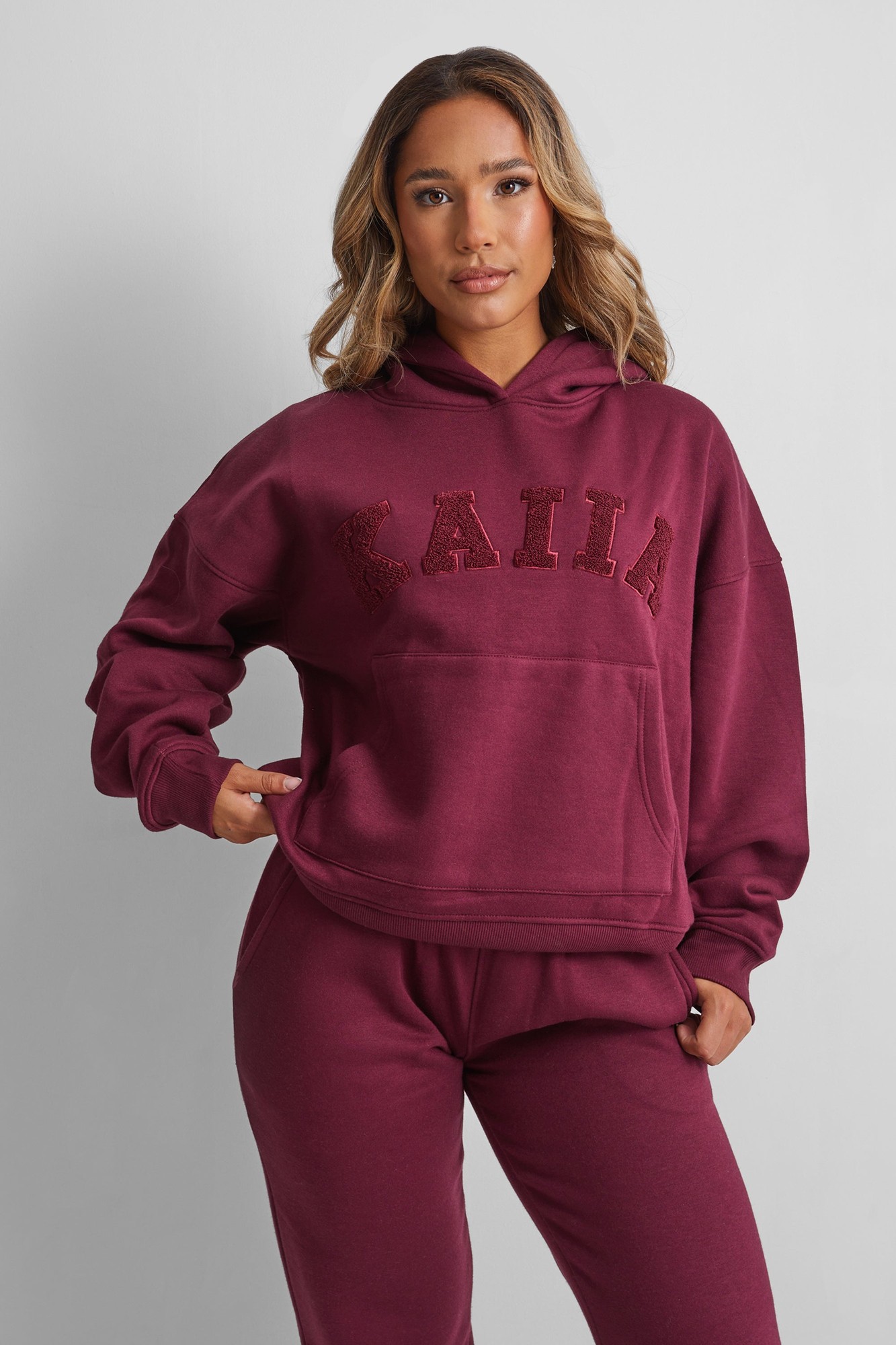 Oversized deep burgundy hoodie featuring a textured "KAIIA" slogan, a front pocket, and a relaxed fit, made from soft cotton material.