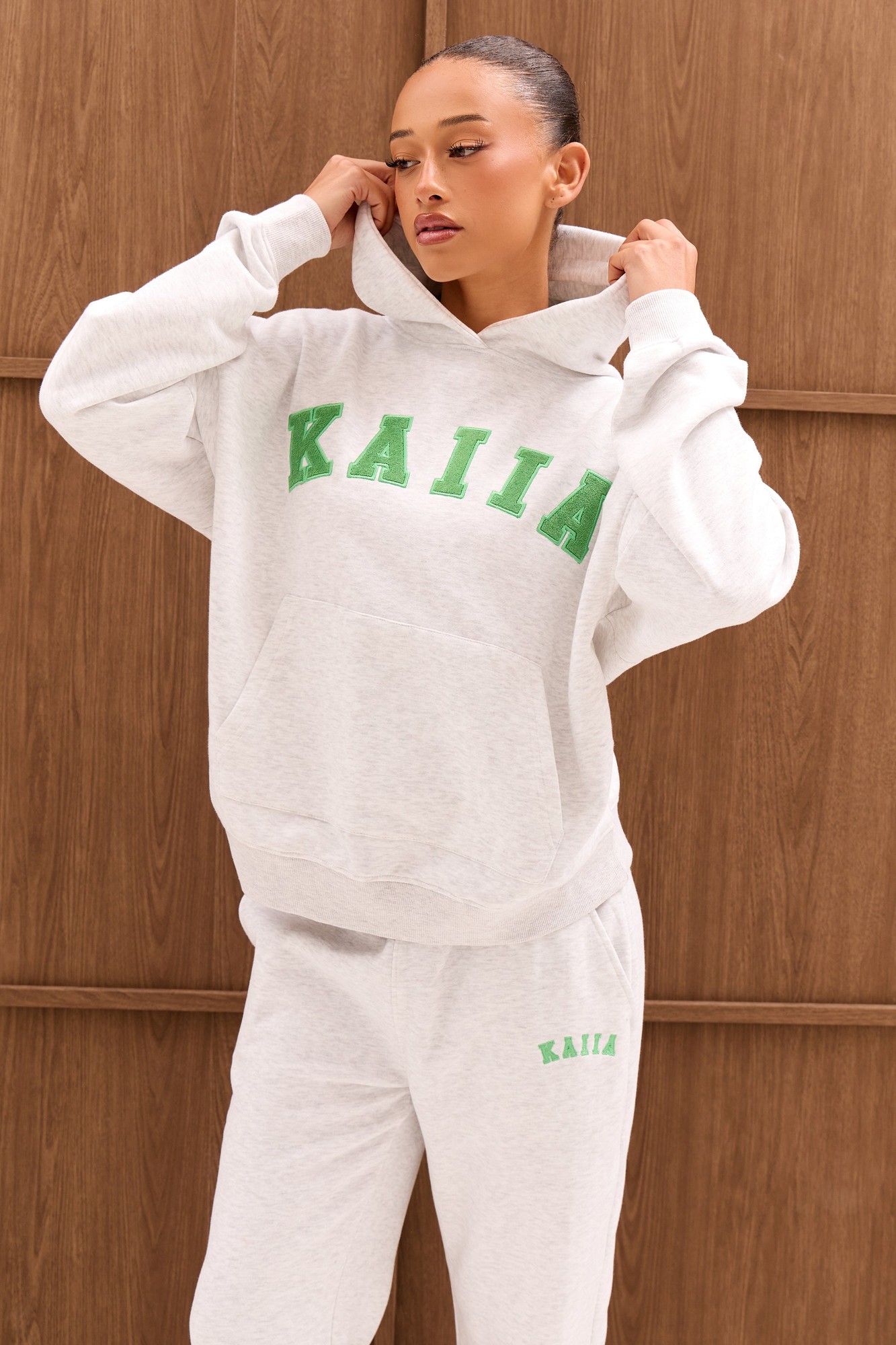 Oversized light grey marl hoodie featuring bold spring green "KAIIA" slogan, with a cozy hood and relaxed fit, styled with matching sweatpants.