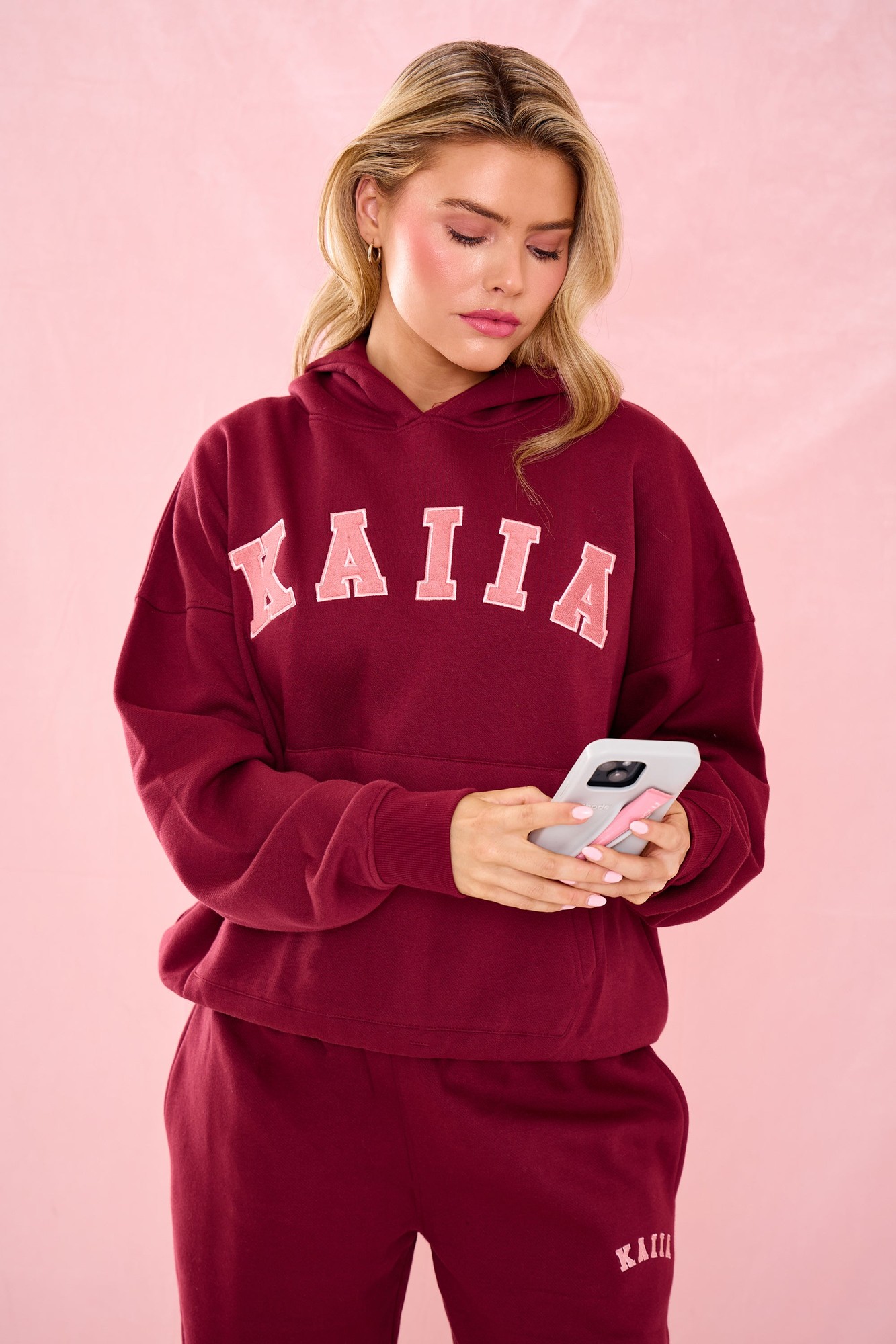 Oversized hoodie in warm berry color, featuring the word "KAIIA" in light pink lettering, made from soft material, paired with matching joggers.