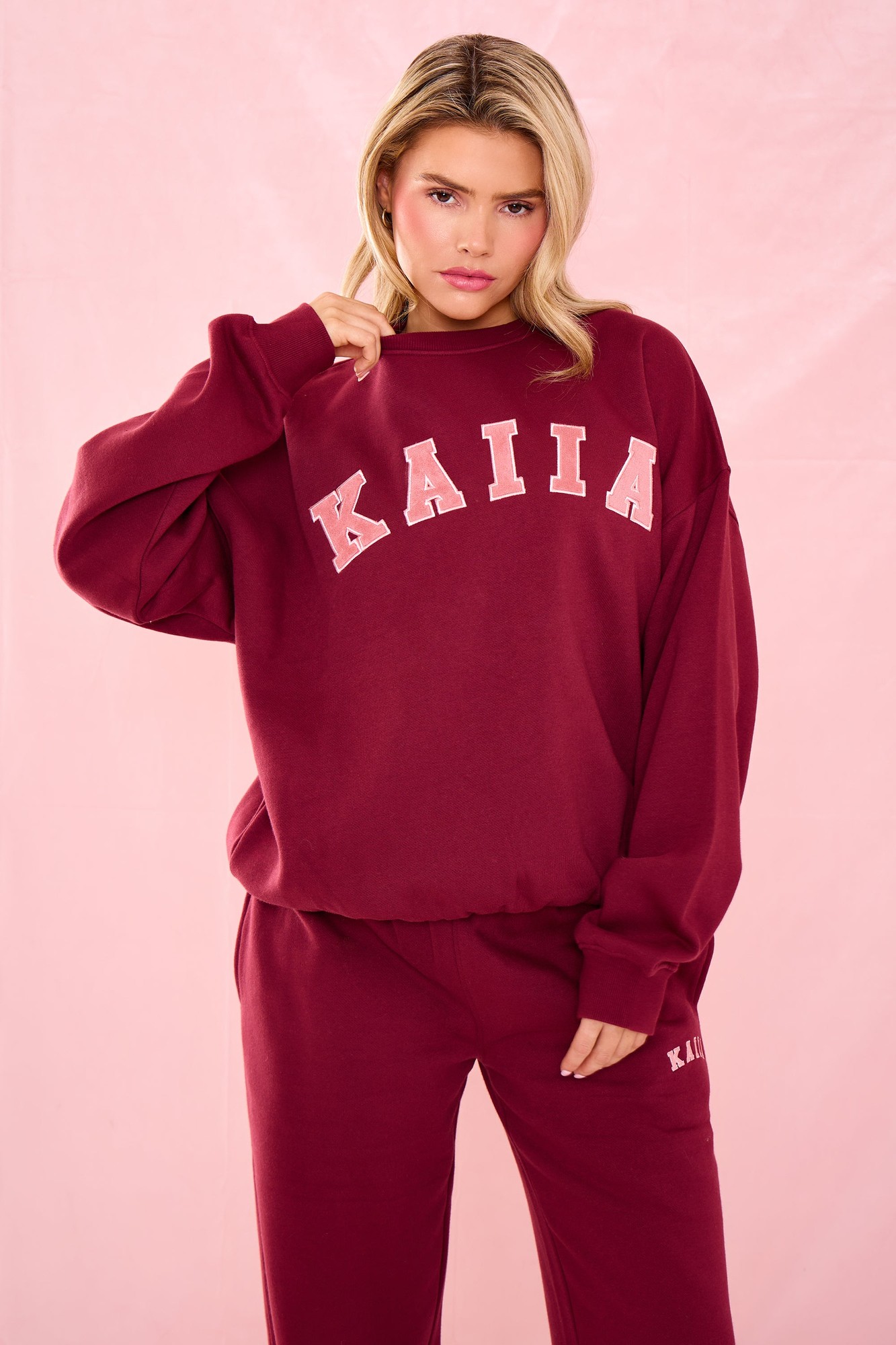 Oversized sweatshirt in warm berry color featuring "KAIIA" slogan in light pink, made from soft material, styled with relaxed fit and dropped shoulders.