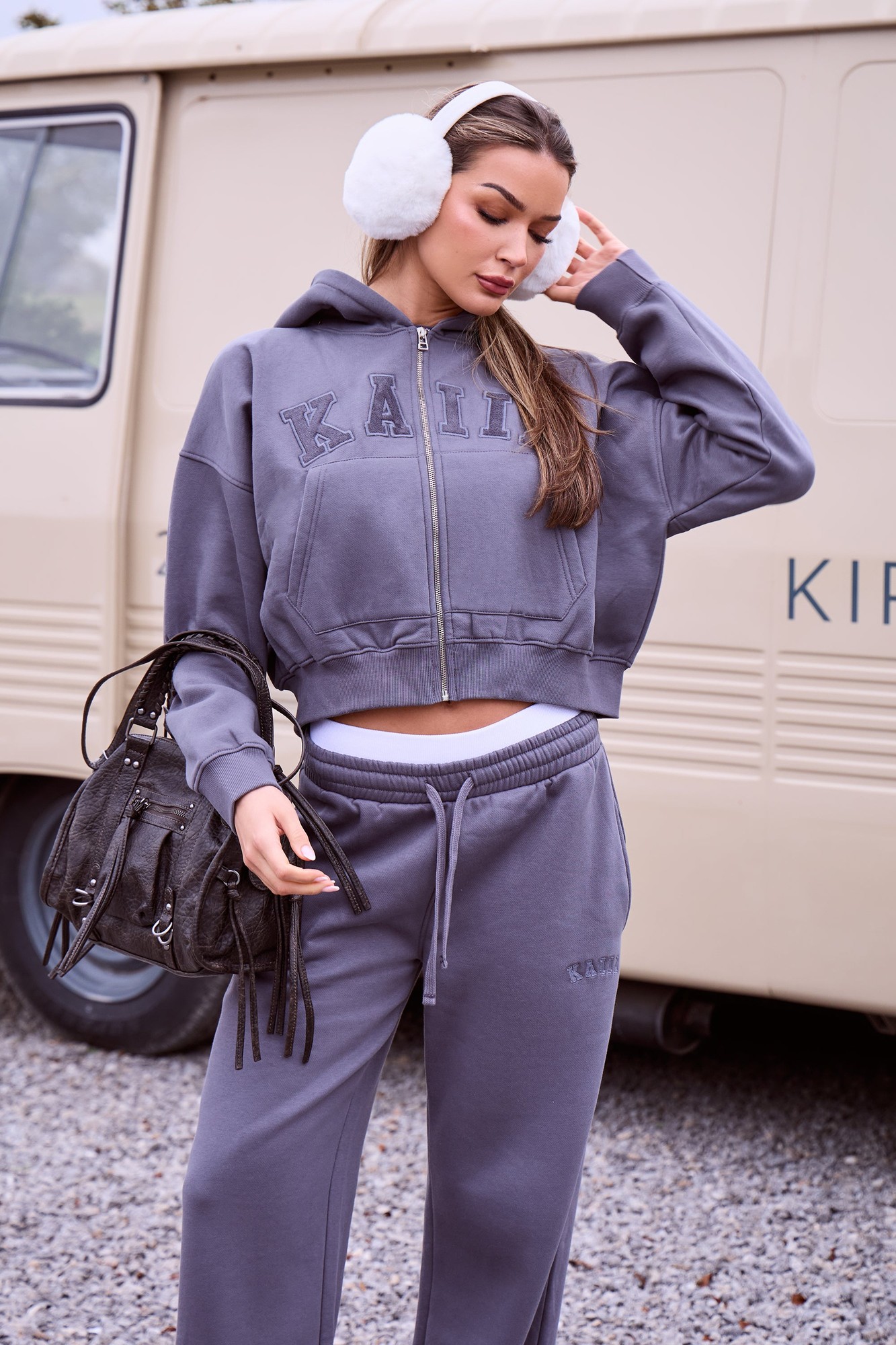 Petrol grey oversized zip-through hoodie with "Kaiia" slogan, soft material, paired with matching sweatpants, and accessorized with white earmuffs and a black handbag.