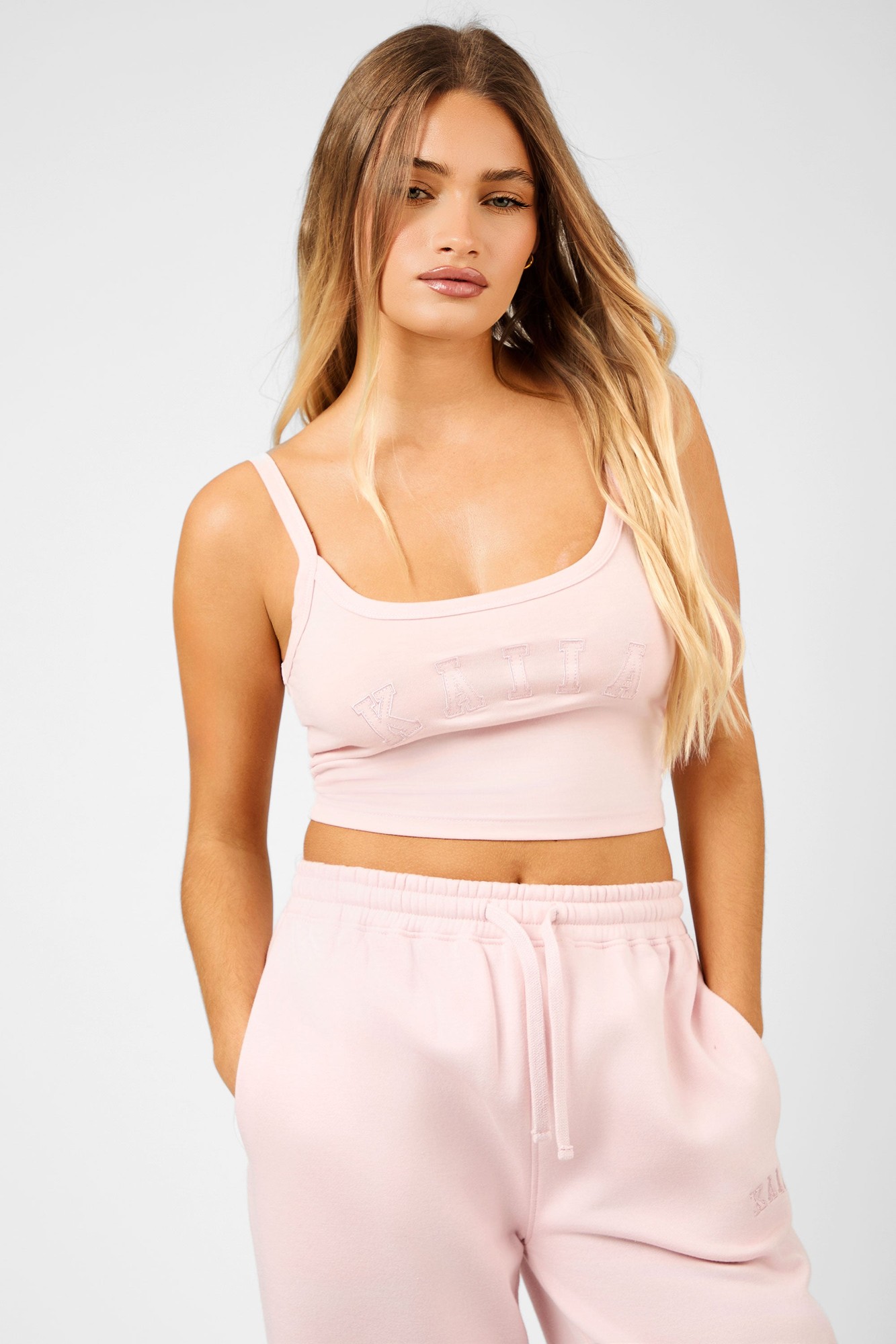 Dusty pink cropped vest top with thin straps, featuring a subtle embossed "Kaiia" slogan on the front, paired with matching light pink sweatpants.