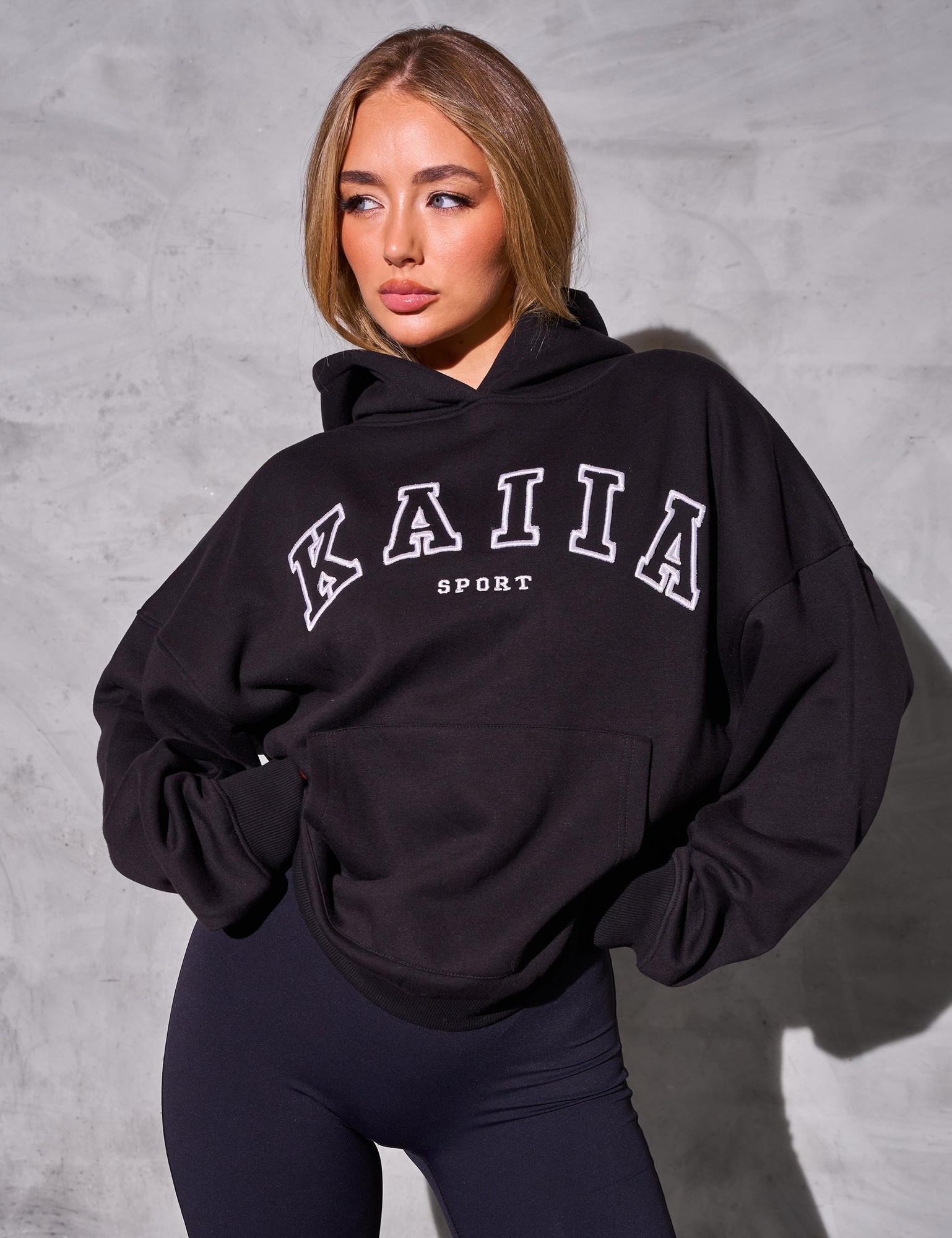 Oversized black hoodie featuring "KAIIA SPORT" in bold white lettering, made from soft material, with a relaxed fit and a drawstring hood.