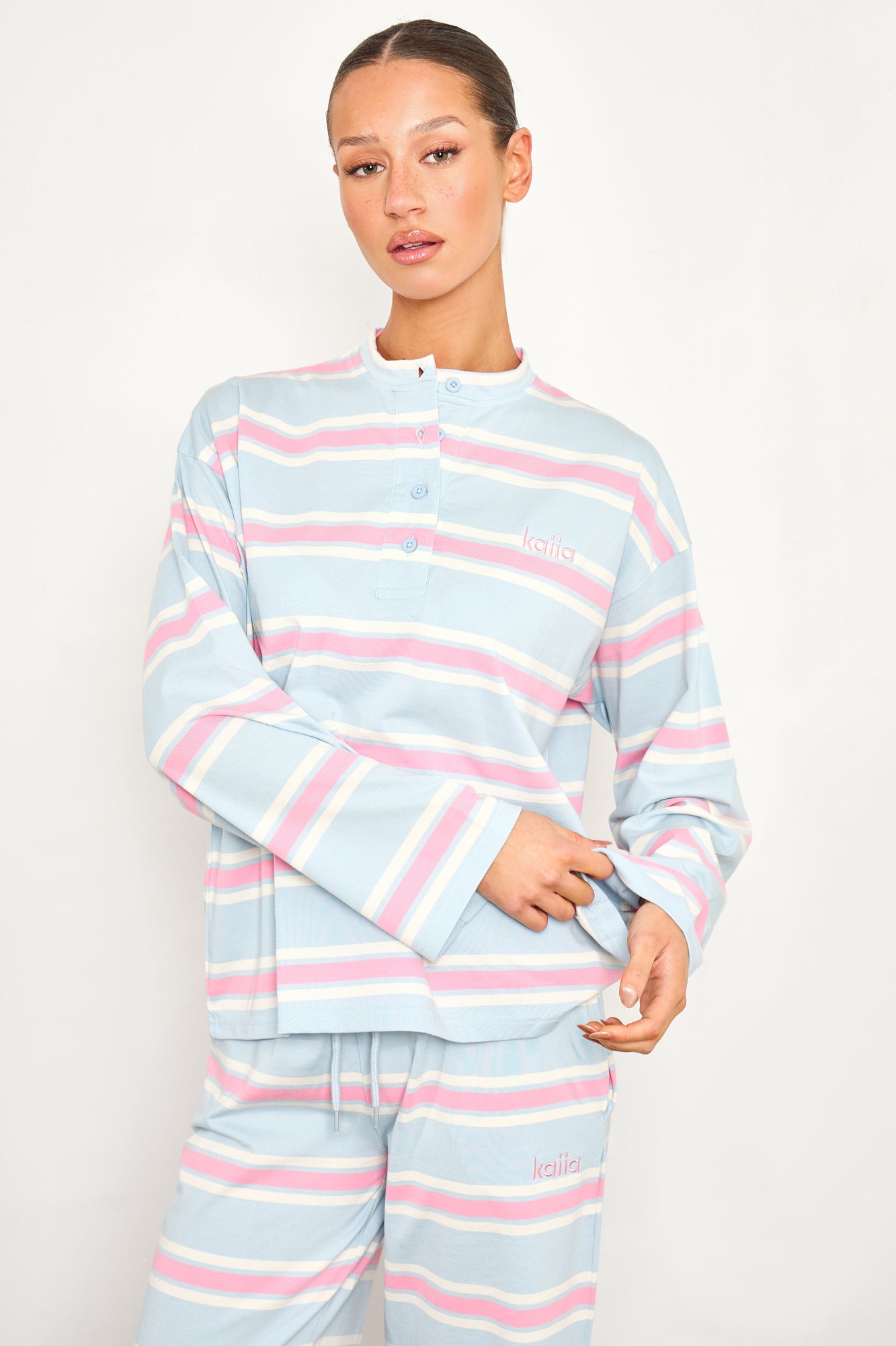 Striped oversized button-up T-shirt in baby pink and baby blue, featuring a relaxed fit, long sleeves, and a small logo on the chest.