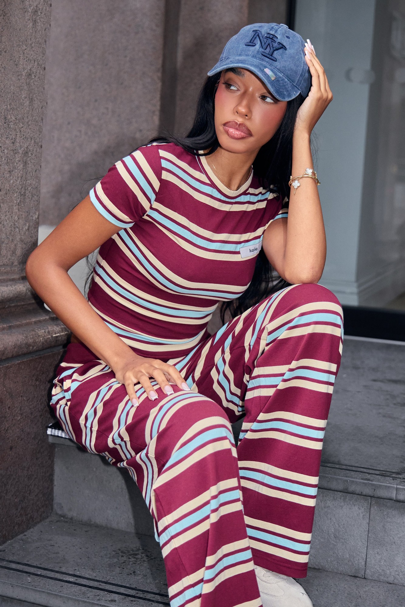 Burgundy and baby blue striped baby tee featuring a label logo, made from soft material, styled with matching pants and a blue cap.