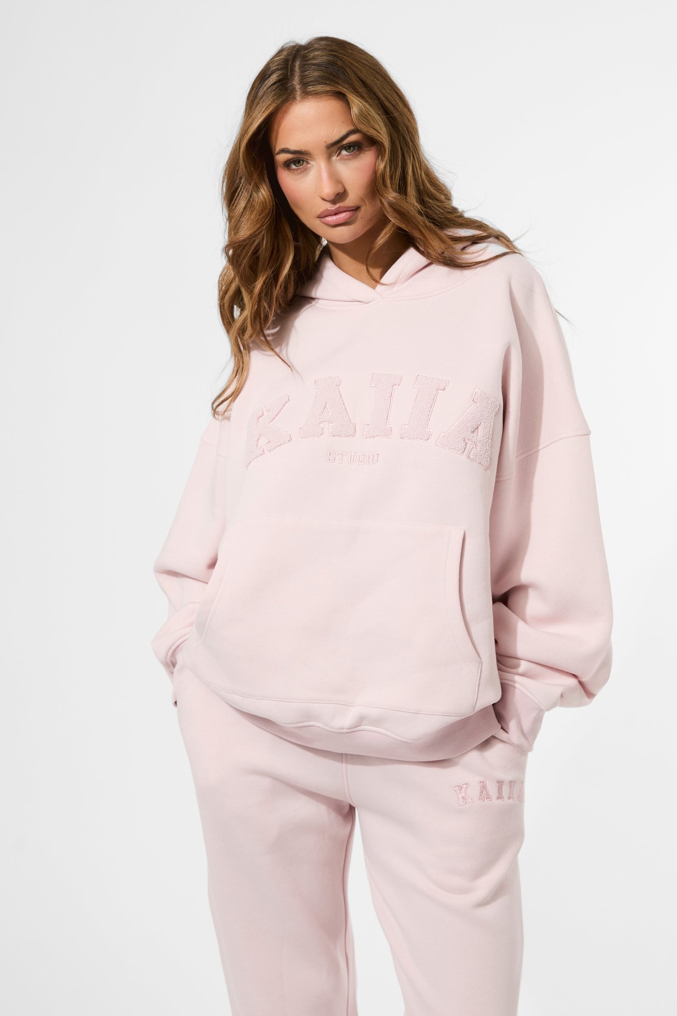 Oversized pink hoodie featuring a textured "KAIIA" slogan on the front, made from soft material, styled with a relaxed fit and a spacious hood.
