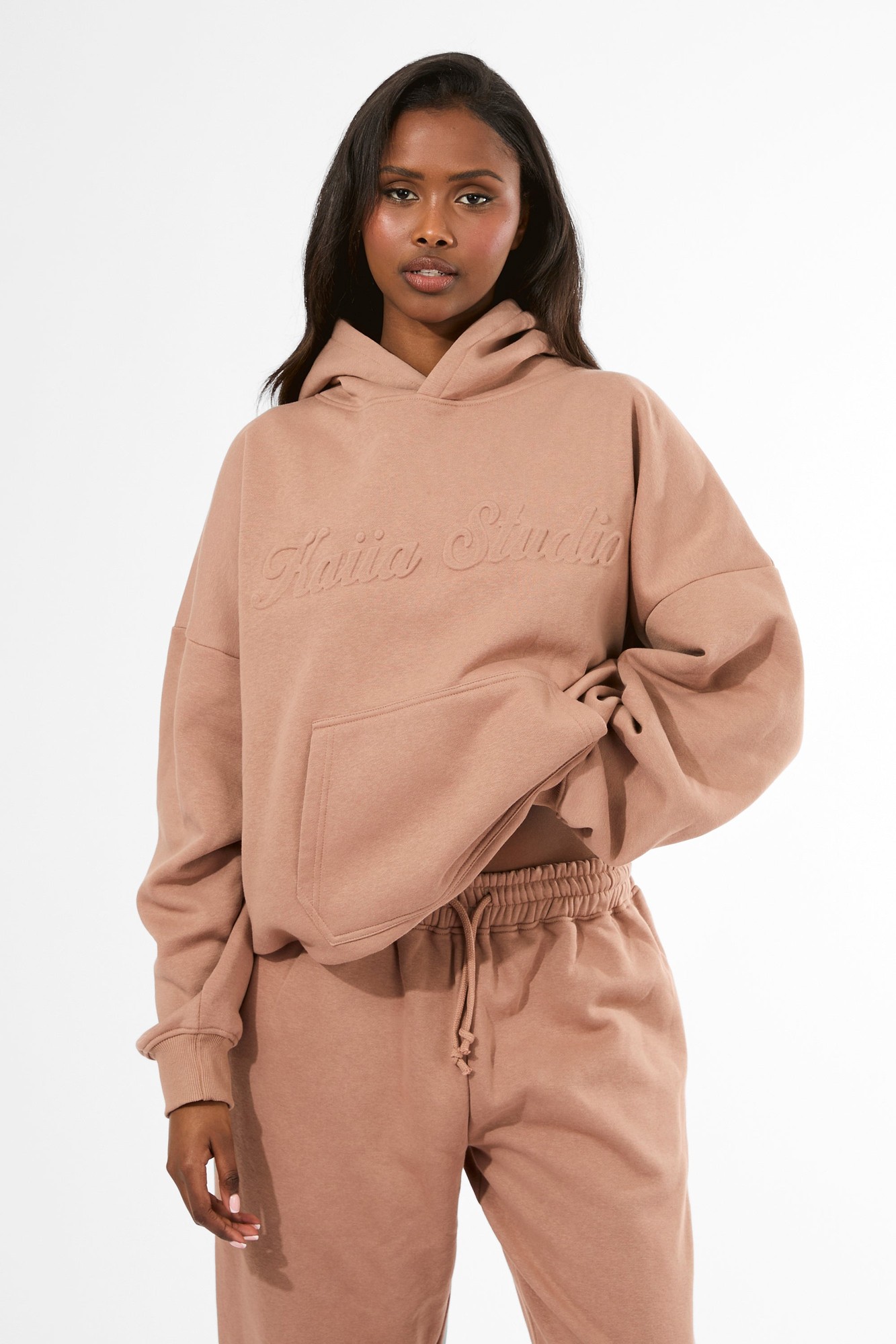 Oversized hoodie in milk chocolate color with an embossed "Kaiia Studio" logo, featuring a front pocket and a relaxed fit, made from soft material.