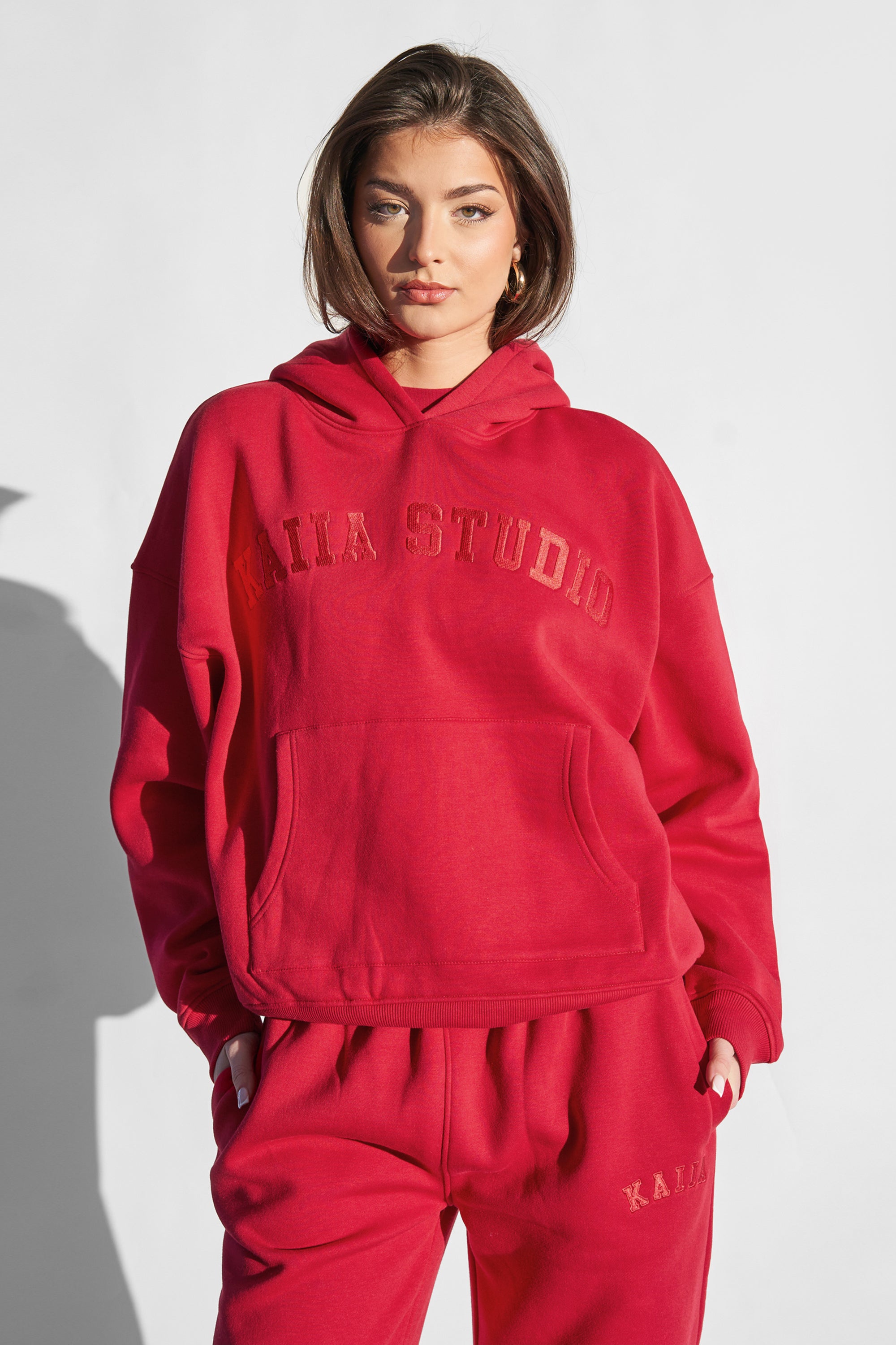 Oversized red hoodie by Kaiia Studio, featuring a front pocket, relaxed fit, and embroidered logo in a slightly darker shade, paired with matching sweatpants.