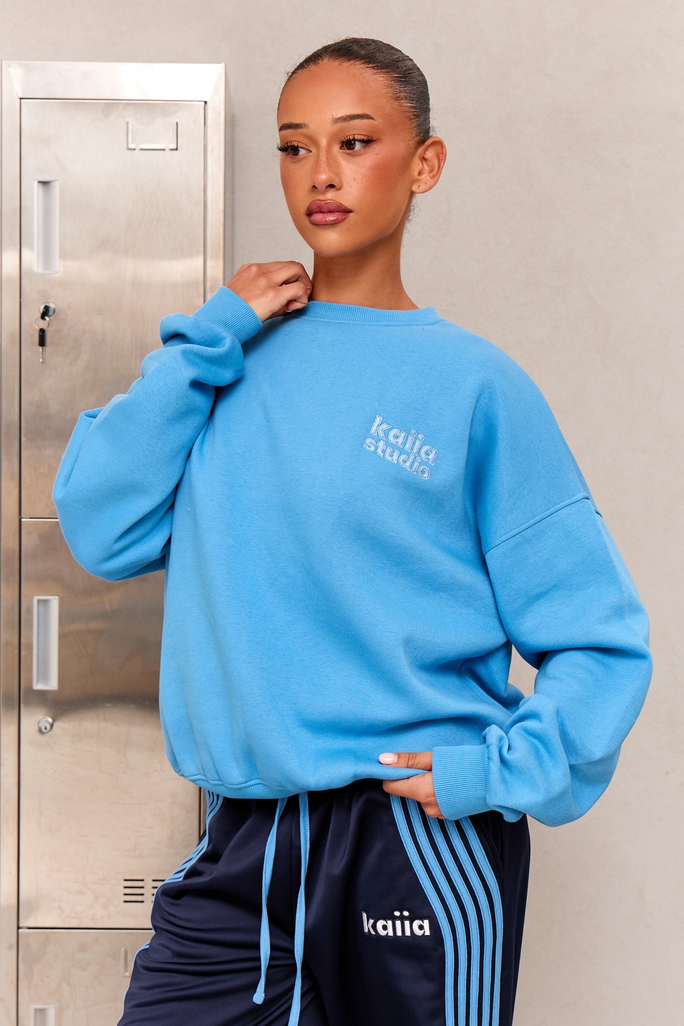 Vibrant blue oversized sweatshirt with a soft material, featuring the "kaiia studio" logo on the chest, styled with navy sweatpants and a sleek hairstyle.
