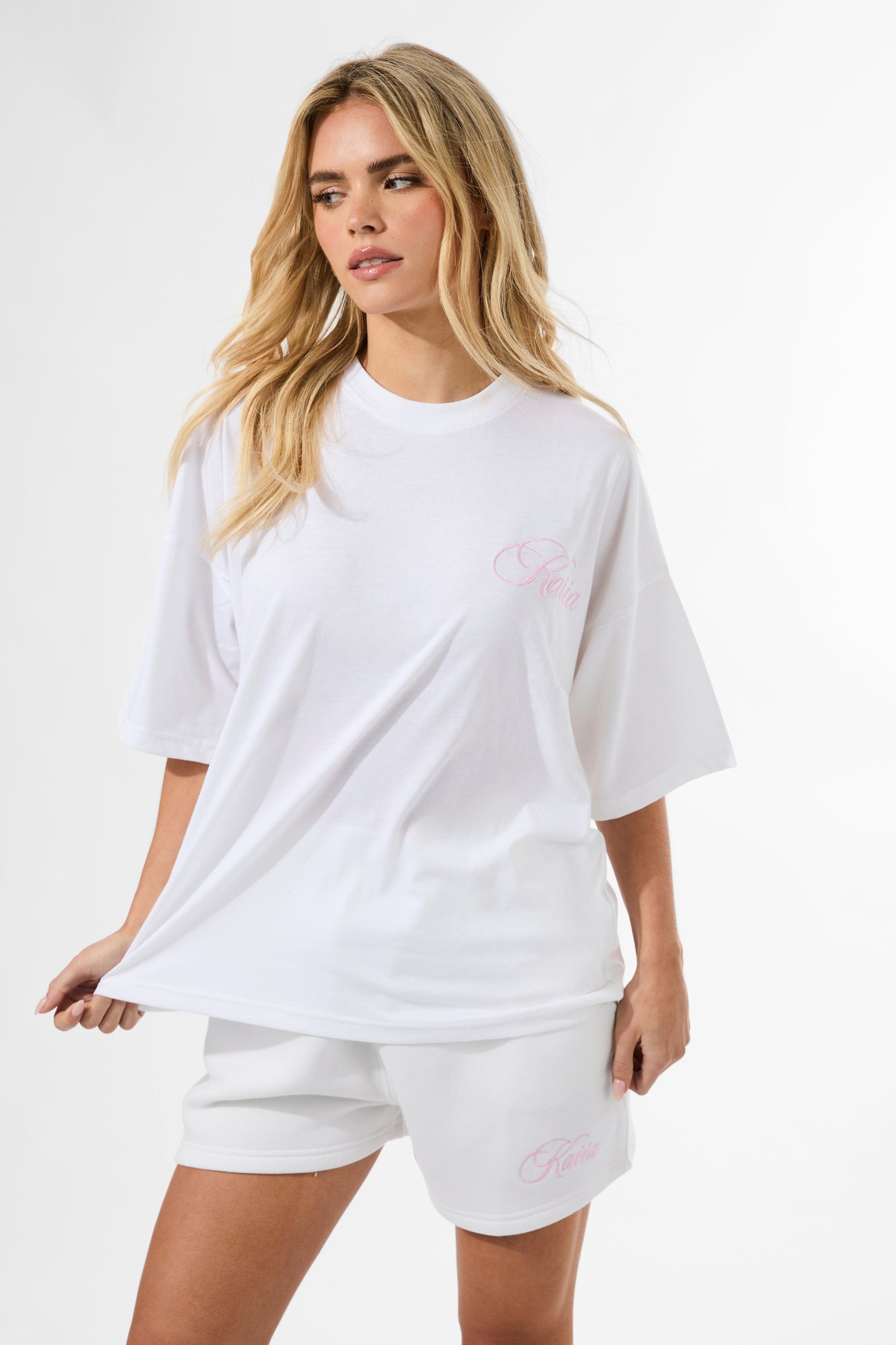 White sweat shorts featuring a pink script logo, made from soft cotton material, with an elastic waistband for comfort.