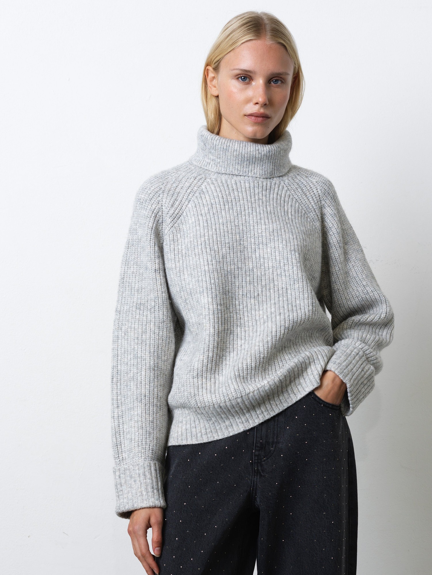 Light grey ribbed knit turtleneck jumper with a relaxed fit, featuring dropped shoulders and long sleeves, styled with dark jeans.