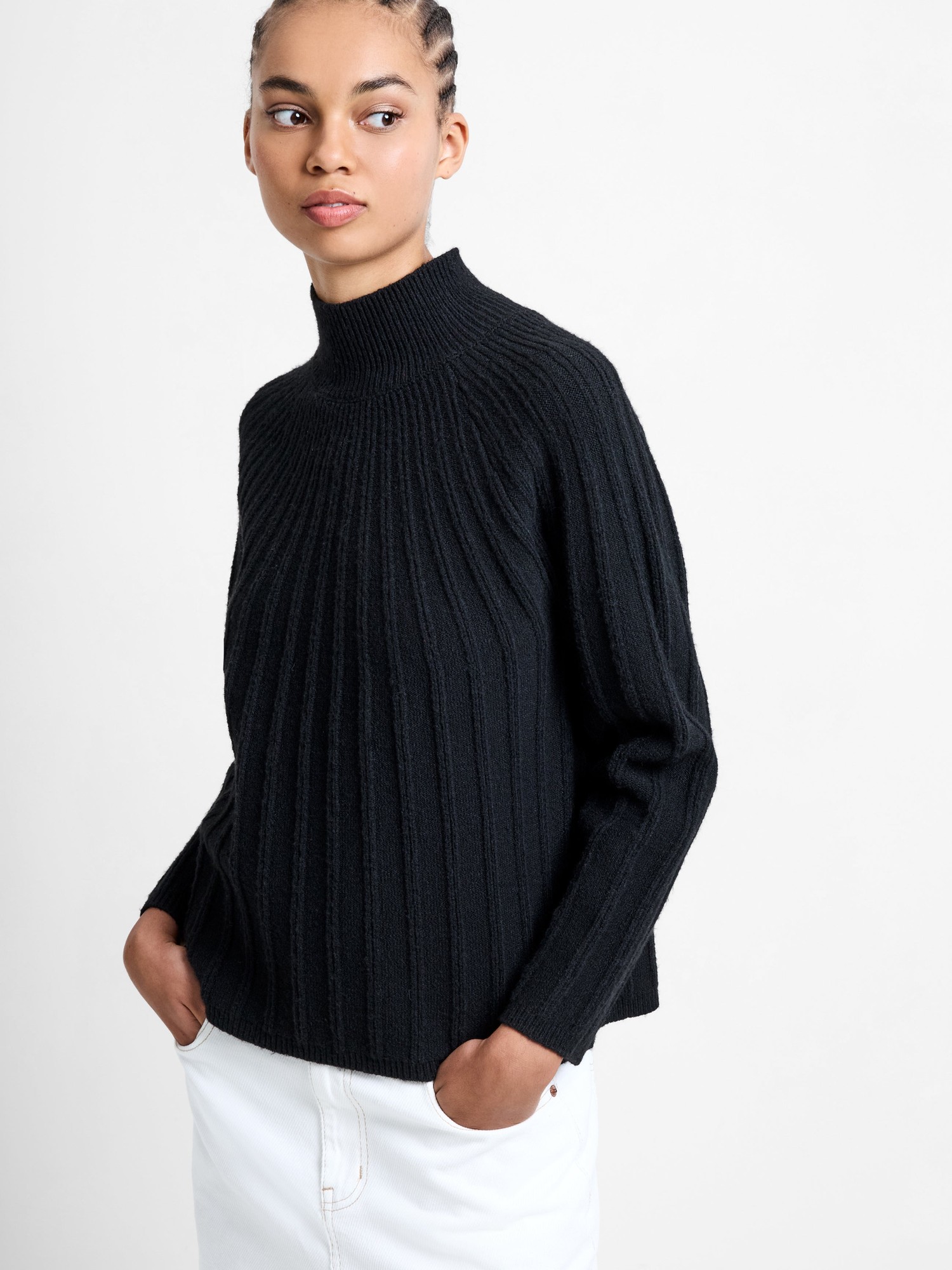Black ribbed mock neck jumper made from recycled material, featuring a relaxed fit and long sleeves, styled with hands in pockets against a neutral background.