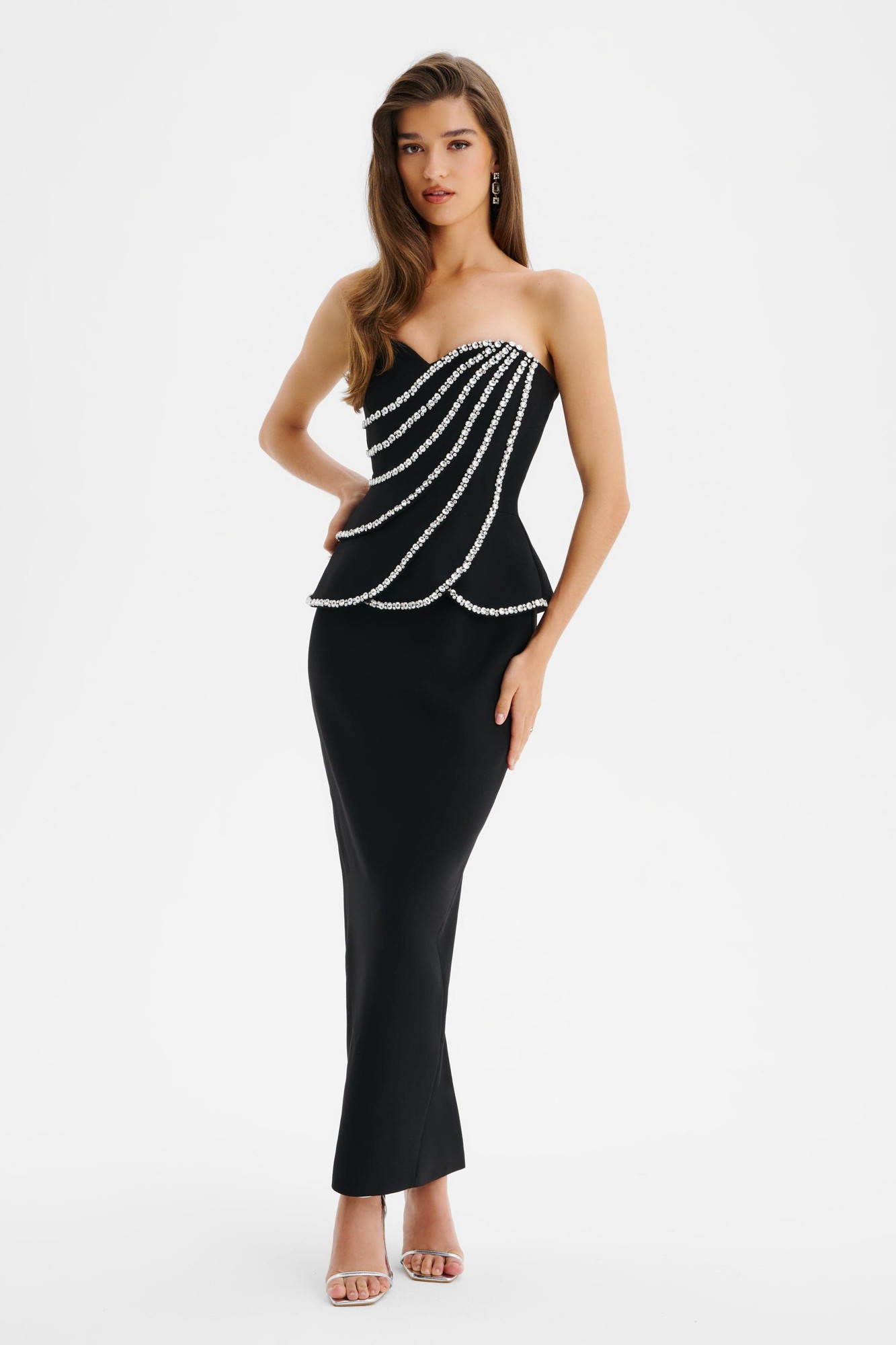 Black midi dress featuring a strapless design, scallop peplum waist, and embellished with diamante detailing across the bodice, made from a sleek material.