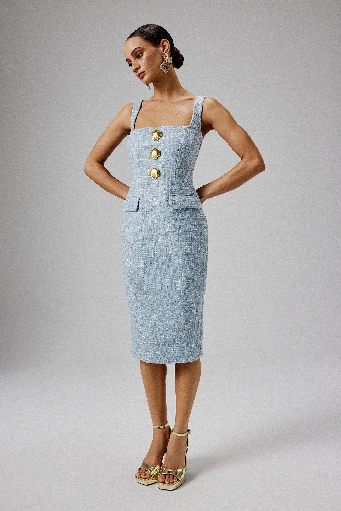 Blue boucle midi dress featuring a square neck, shell embellishments, three large buttons, and two front pockets, styled with strappy heels and statement earrings.