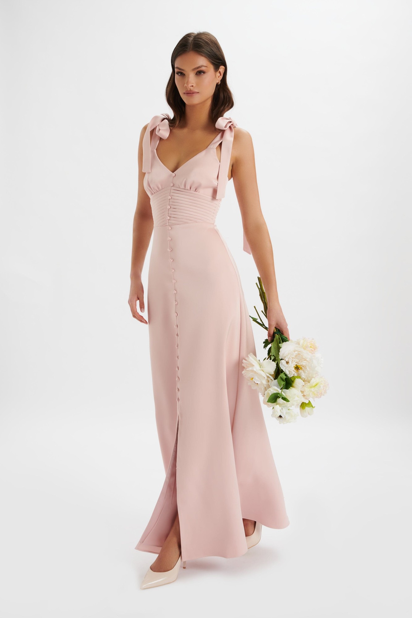 Pink satin maxi dress with tie shoulder straps, ruched bodice, and button detailing down the front, paired with a bouquet of flowers.