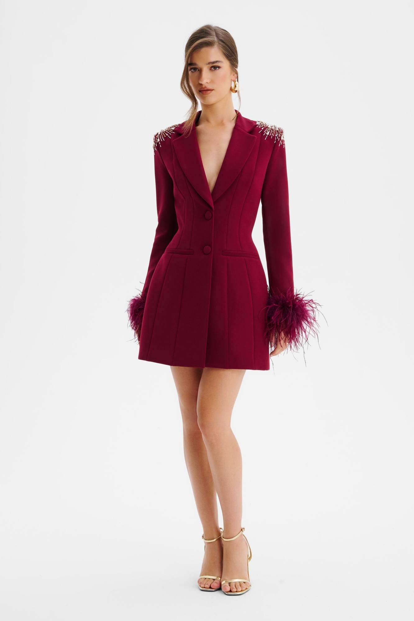 Burgundy blazer dress featuring star embellishments, feather cuffs, a tailored silhouette, and a deep V-neckline, styled with gold strappy heels.