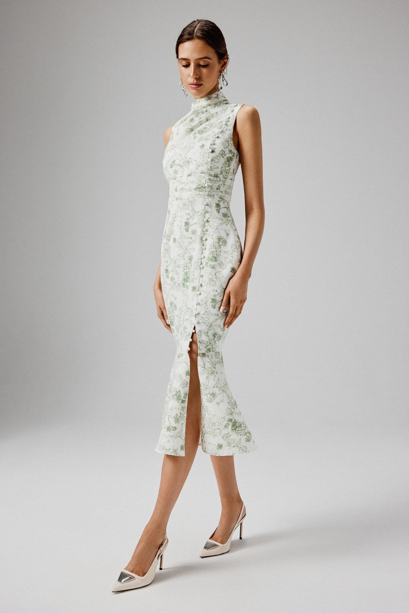 High neck midi dress in sage porcelain print, featuring a fitted silhouette, side slit, and crepe material, styled with elegant earrings and pointed-toe heels.