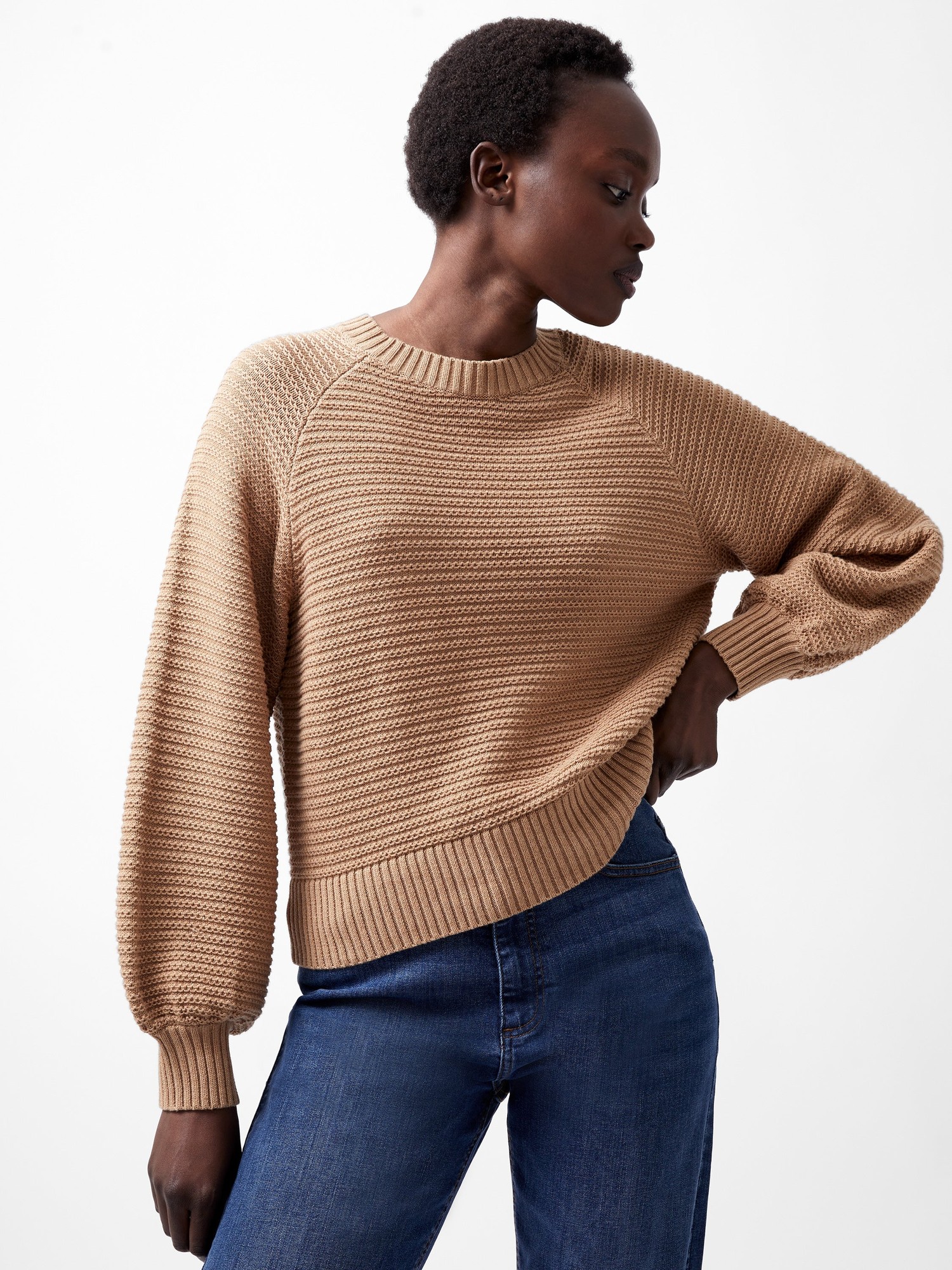 Camel-colored knitted jumper with bishop sleeves, featuring a textured pattern and ribbed hem, paired with blue denim jeans.