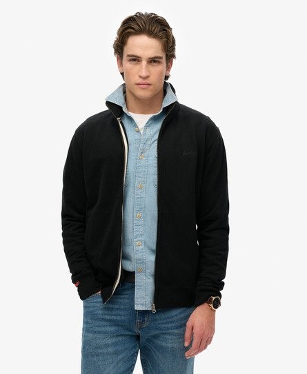 Black tracksuit jacket with a zip front, featuring a high collar and subtle Superdry logo, paired with a light blue button-up shirt and denim jeans.