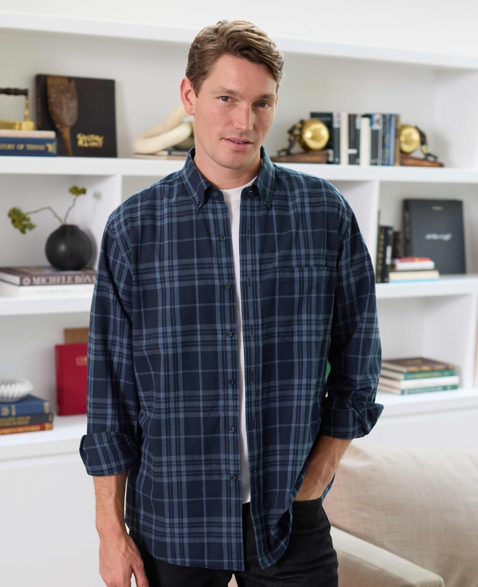 Men's blue brushed cotton check shirt in classic fit, featuring a button-down collar and long sleeves, displayed on a model against a bookshelf background.