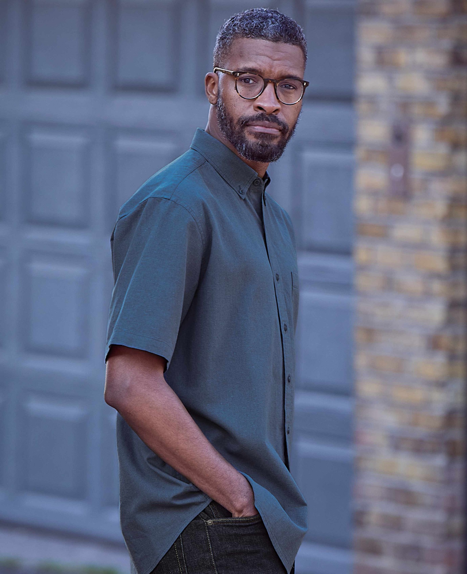 Men's dark blue linen cotton button-down short sleeve shirt with a classic fit, featuring a collar and a chest pocket, displayed on a model against a textured background.
