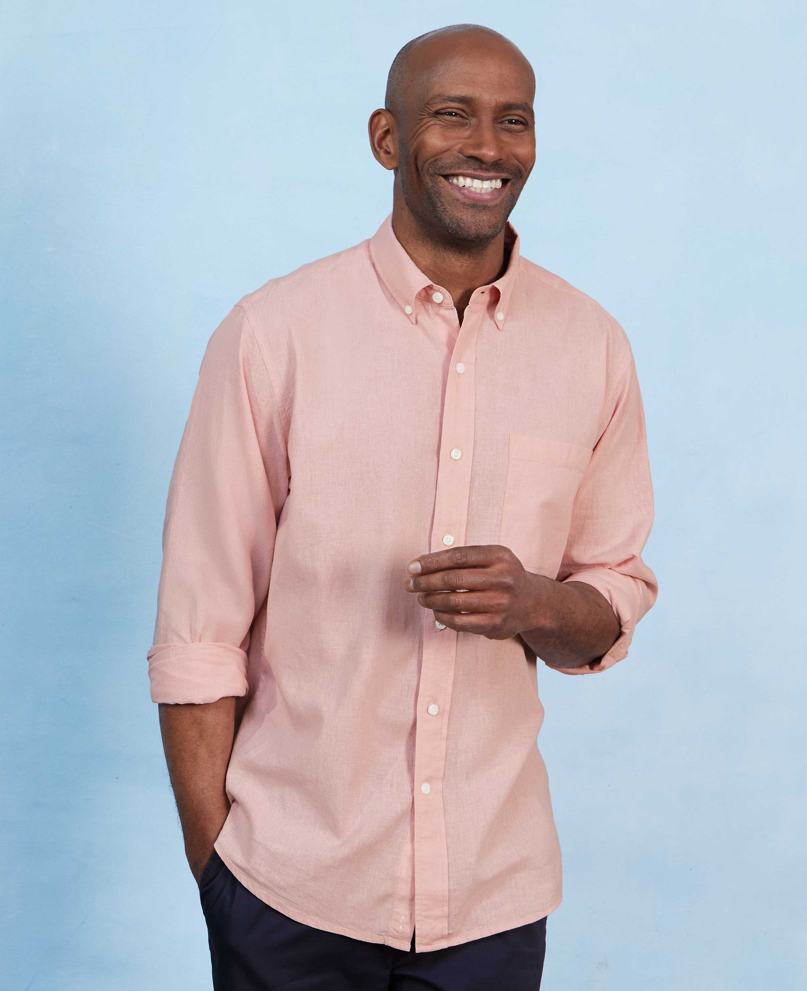Peach linen cotton button-down shirt with a classic fit, featuring a chest pocket and rolled-up sleeves, modeled by a smiling man against a light blue background.