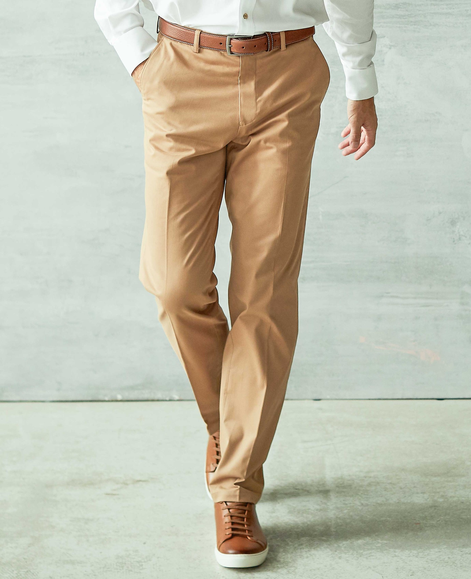 Men's tan stretch cotton chinos with a classic fit, flat front design, featuring side pockets and a smooth finish, paired with a brown belt and white shirt. Size 34" x 32".