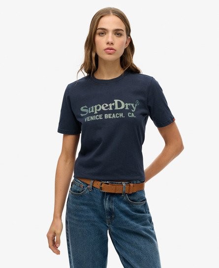 Navy metallic casual T-shirt for women featuring "SuperDry Venice Beach, CA" logo, short sleeves, and a classic fit, paired with high-waisted blue jeans and a brown belt.