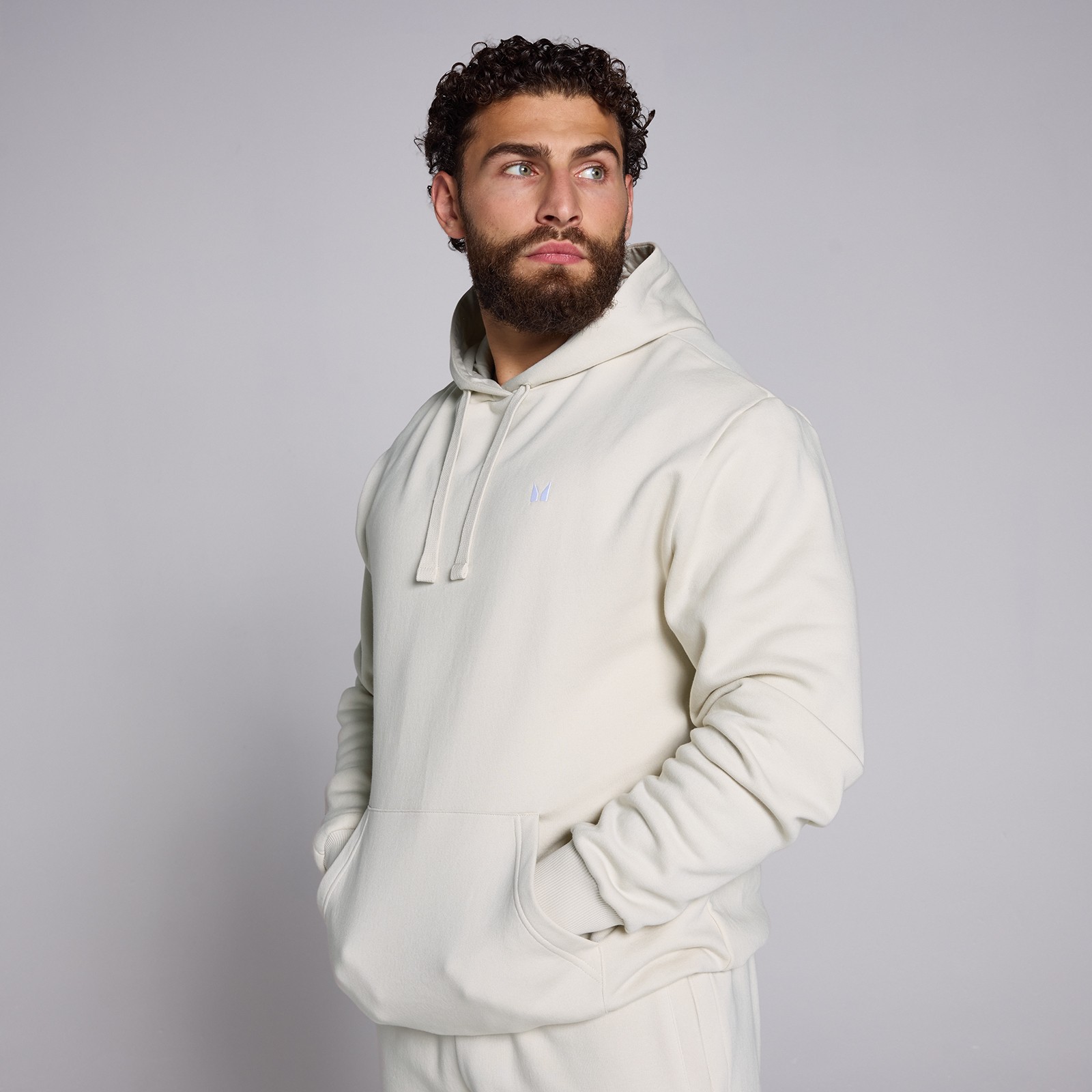 Beige MP Heren Rest Day Hoodie in XXL, featuring a soft material, front pockets, and a drawstring hood, worn by a model with curly hair and a beard.